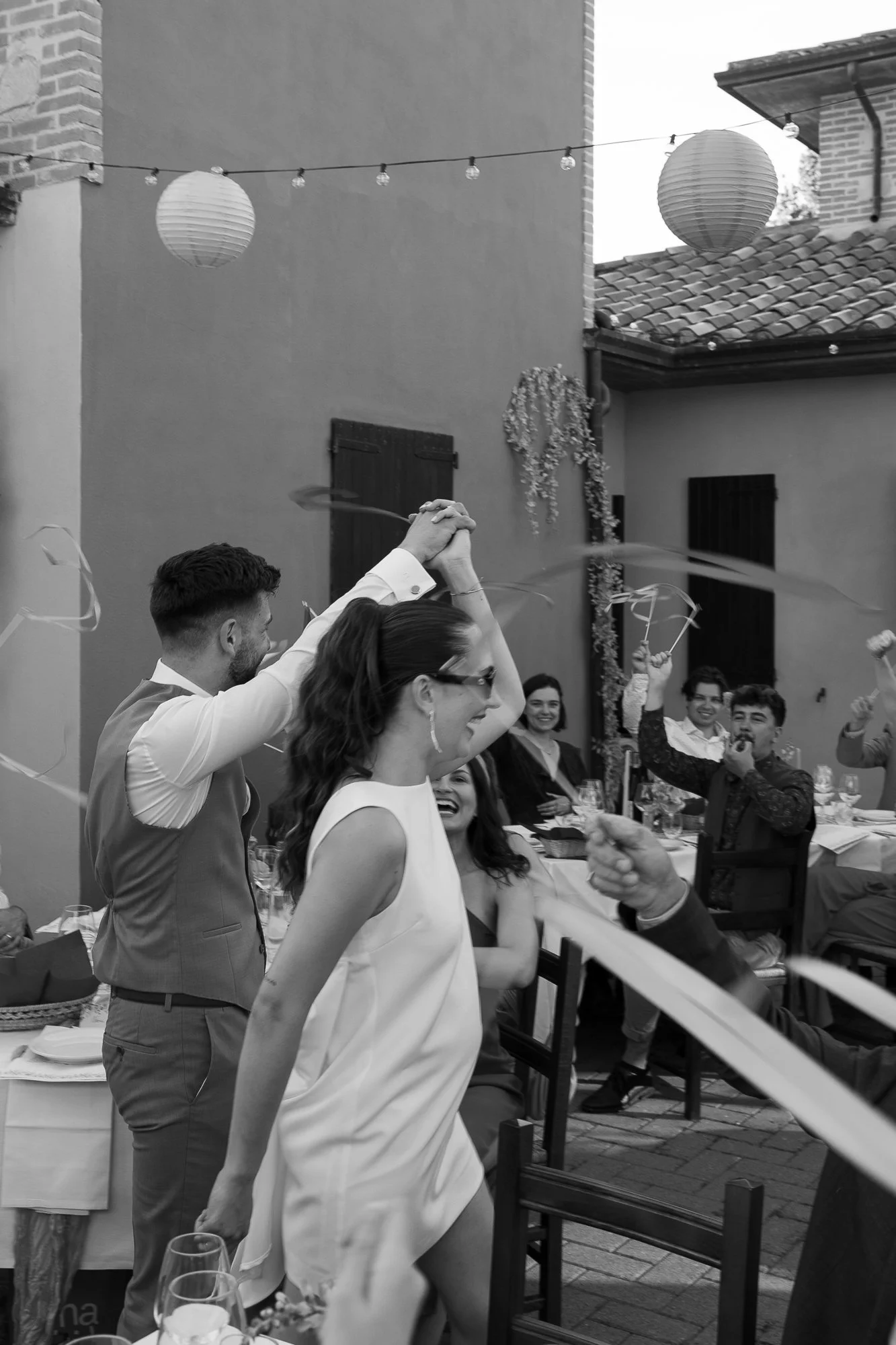 Menschen beim Feiern bei einer Party im Freien, mit Laternen und Dekorationen, lachen und tanzen.