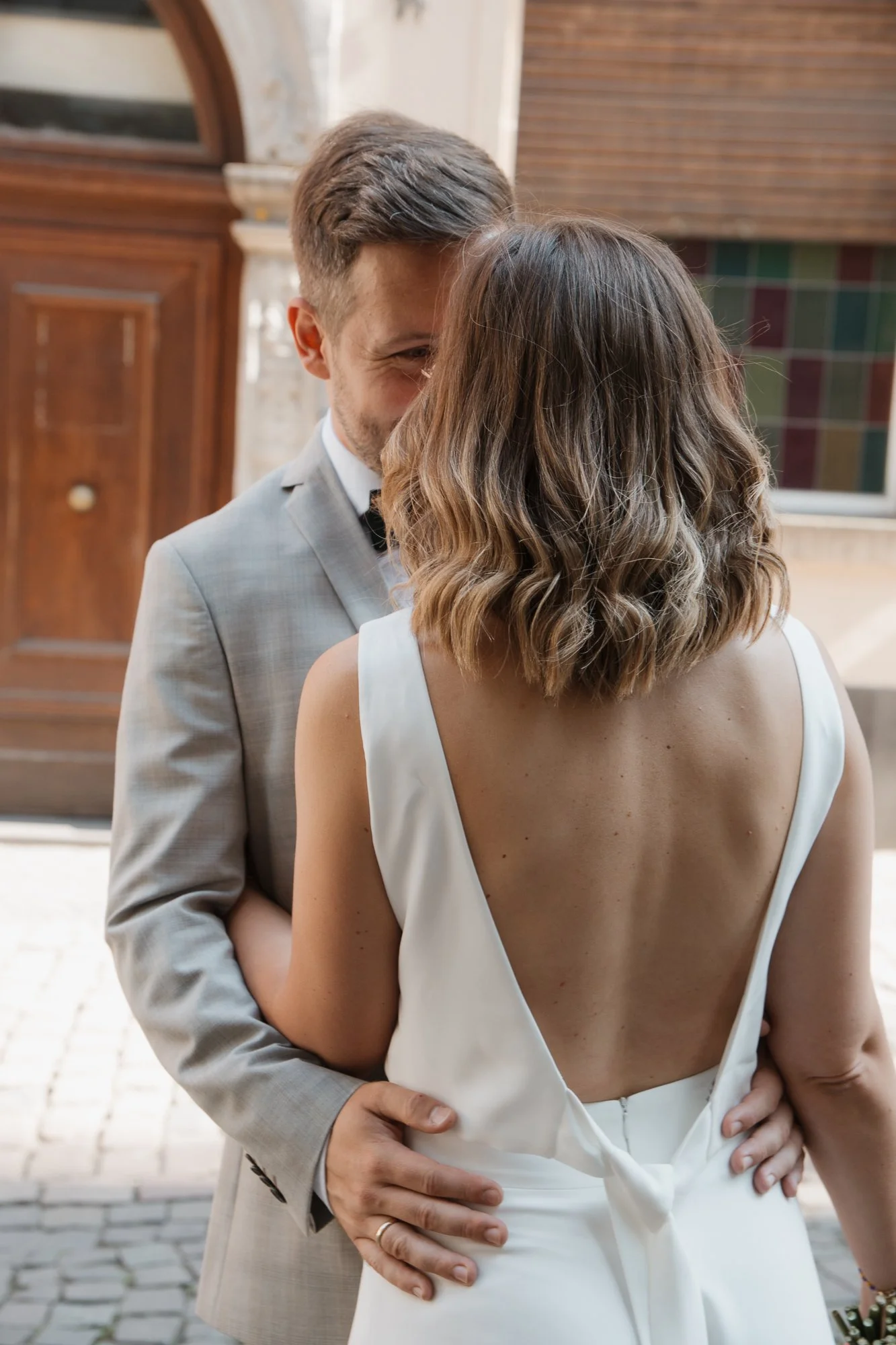 Ein Mann in einem grauen Anzug und eine Frau in einem weißen Kleid stehen sich nahe bei einer Hochzeit, umarmt und küsst.