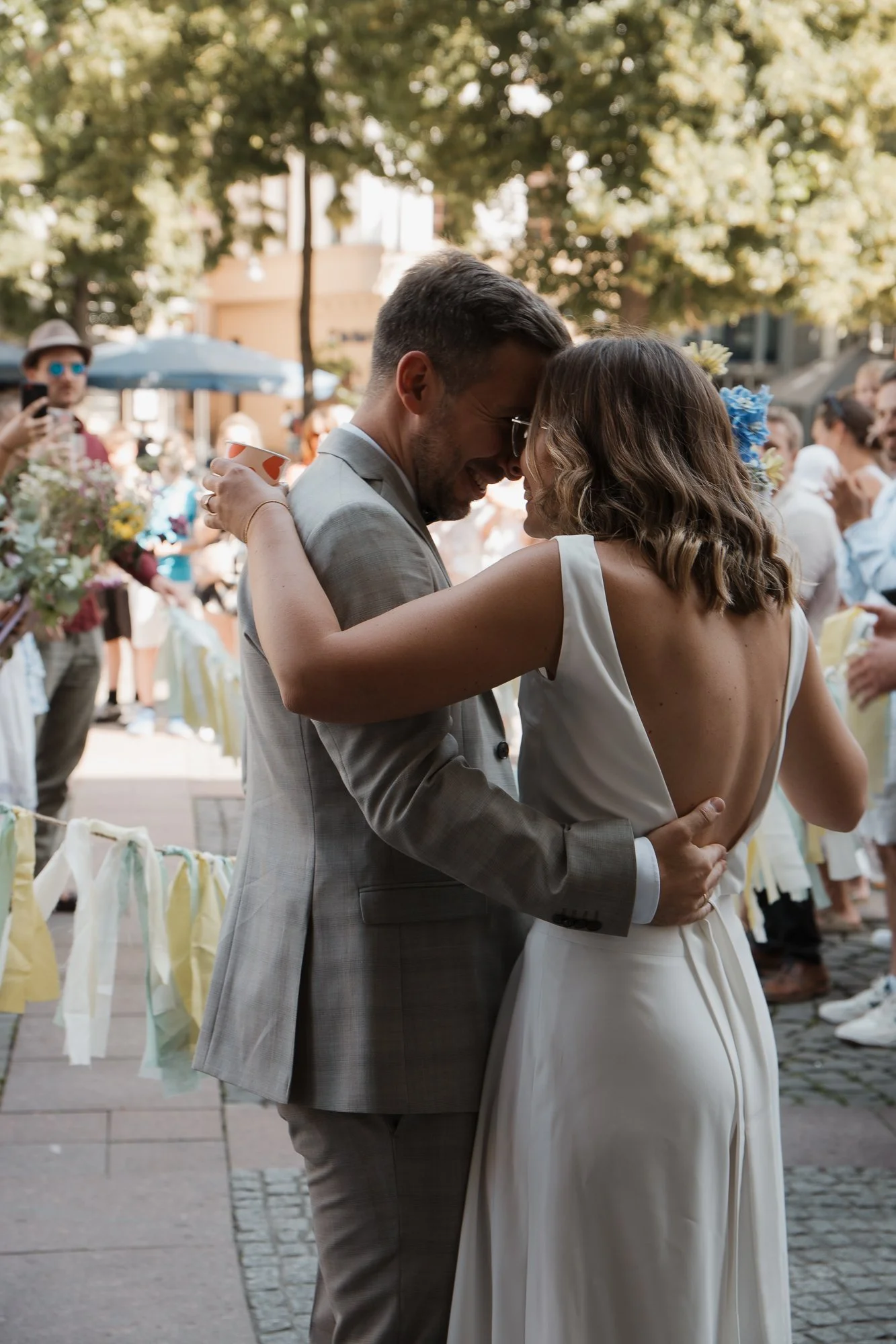Ein Paar bei einer Hochzeit umarmt sich im Freien, umgeben von Gästen und Dekorationen.