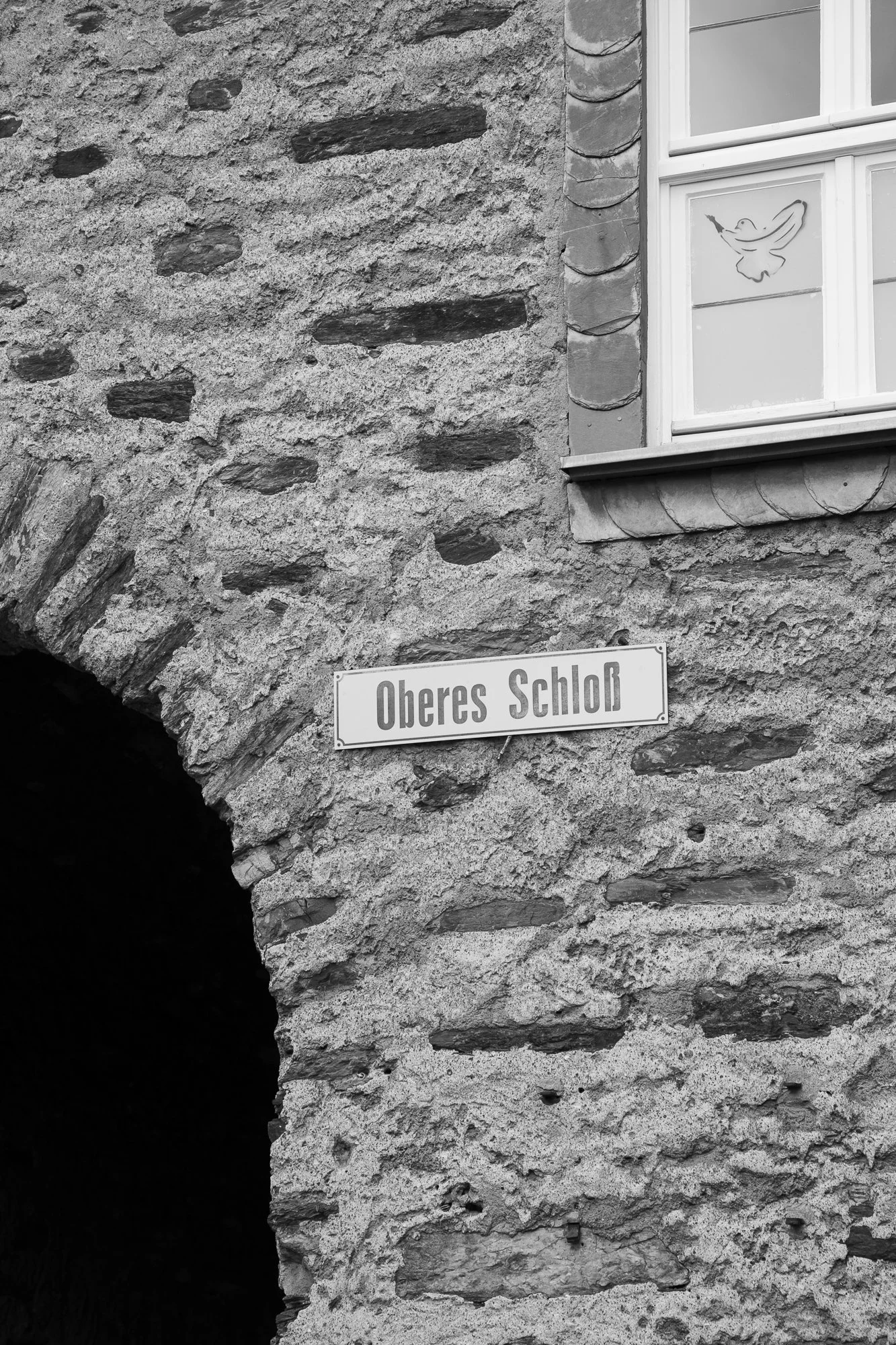 Ein Bild eines Steinhauses mit einem Fenster und einem Straßenschild, das 'Oberes Schloß' heißt.