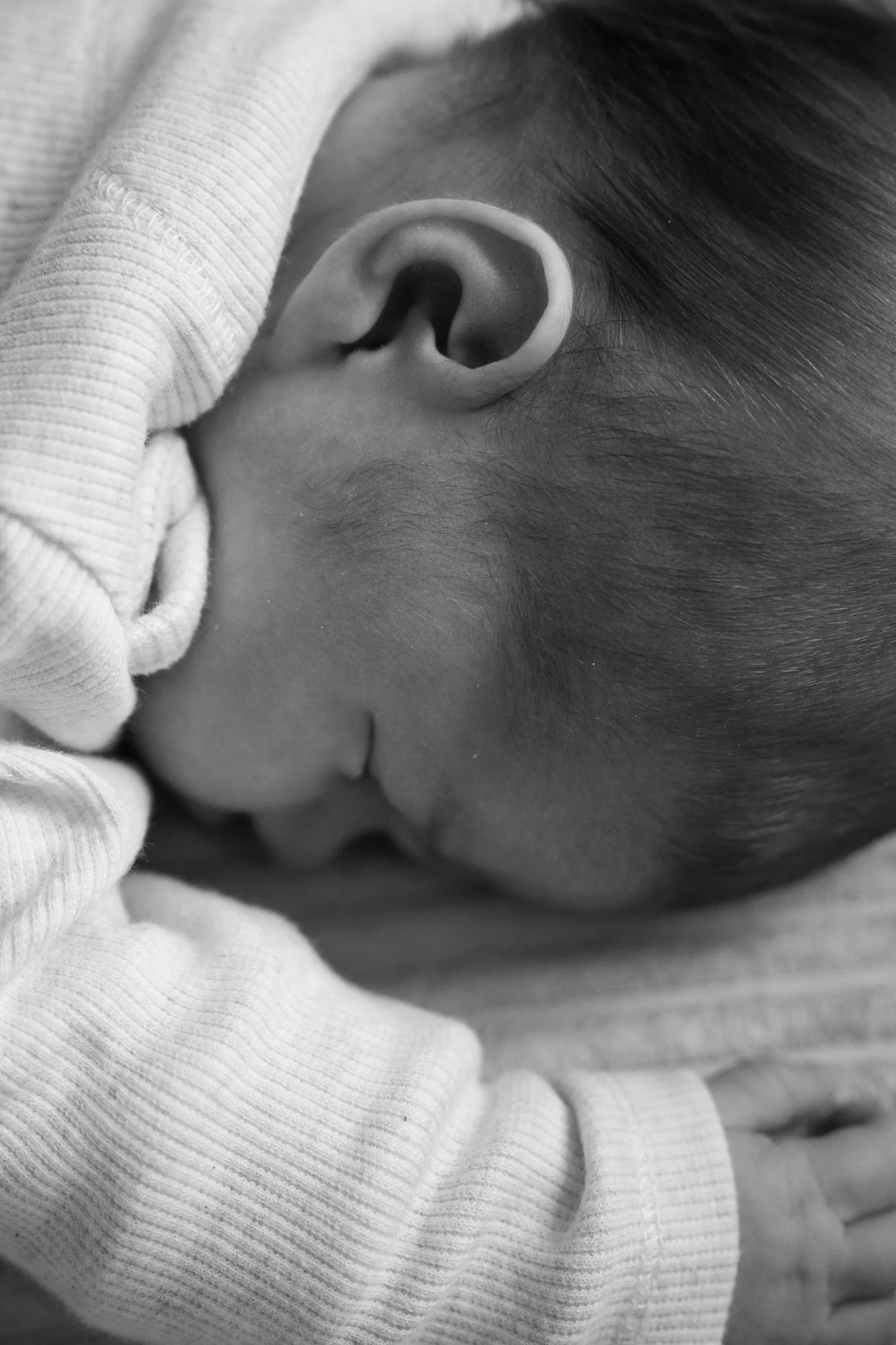 Ein neugeborenes Baby schläft nah an einer Person, die es liebevoll hält, im Schwarz-Weiß-Foto.