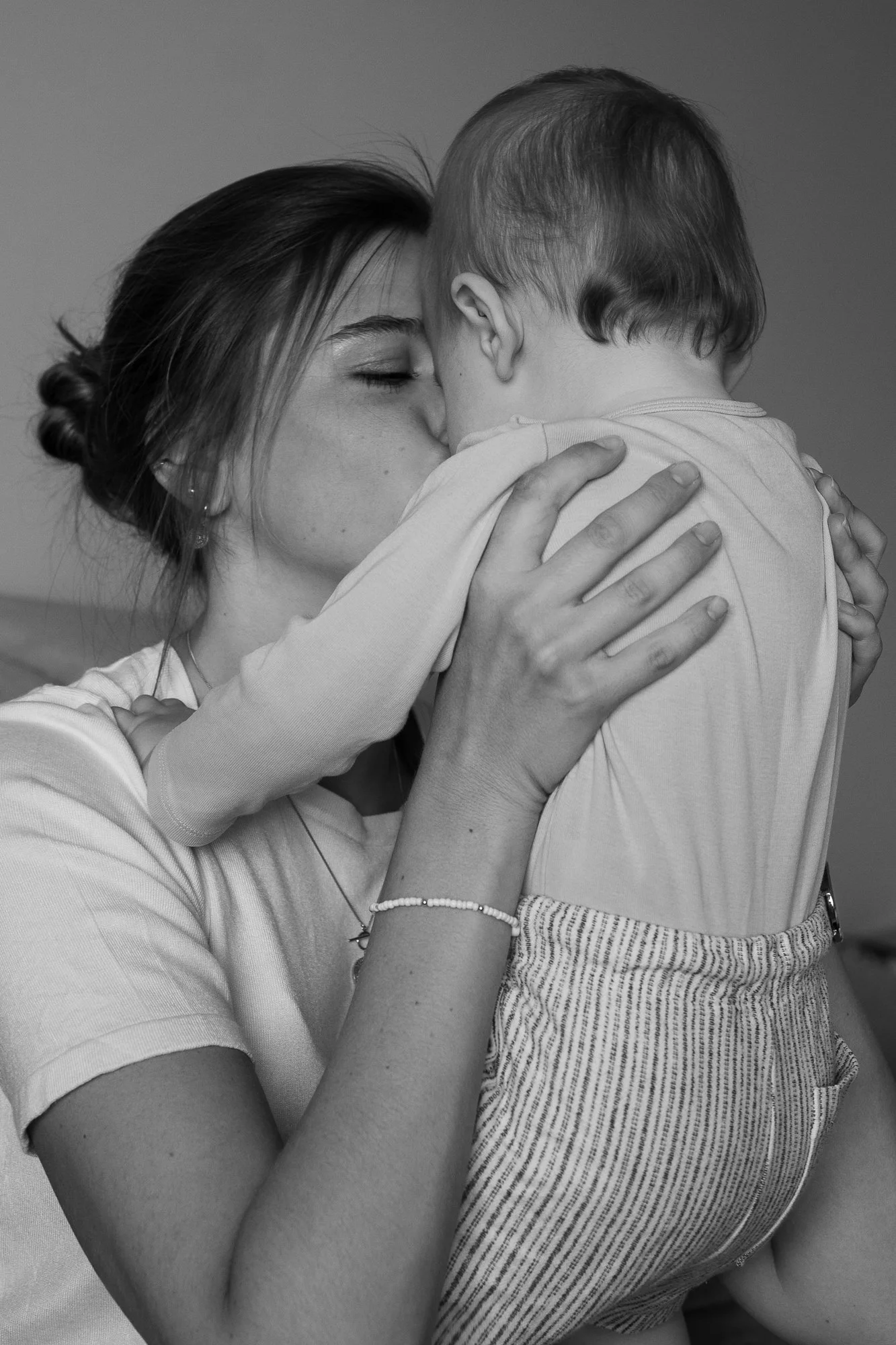Eine junge Frau hält ein Kind im Arm, sie küssen sich auf die Wange, Schwarz-Weiß-Foto.