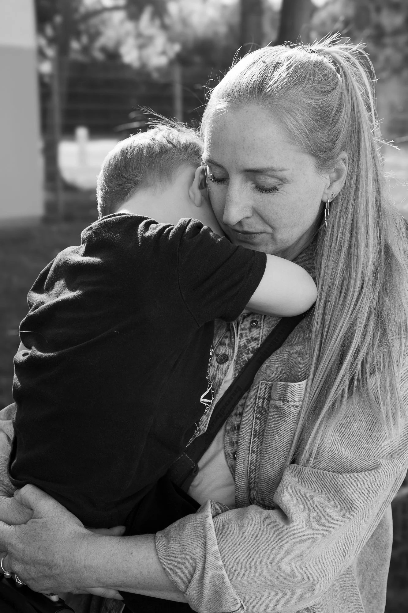 Ein Mädchen umarmt eine Frau, vermutlich ihre Mutter, auf einem Außengelände. Das Bild ist in Schwarz-Weiß.