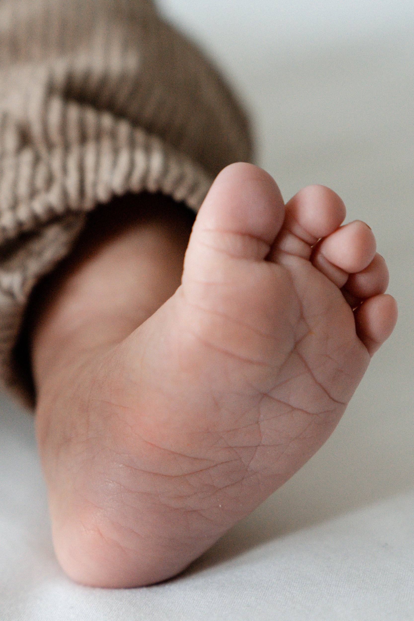 Nahaufnahme eines Babyfusses, teilweise eingekleidet in einen gestreiften Strampler.