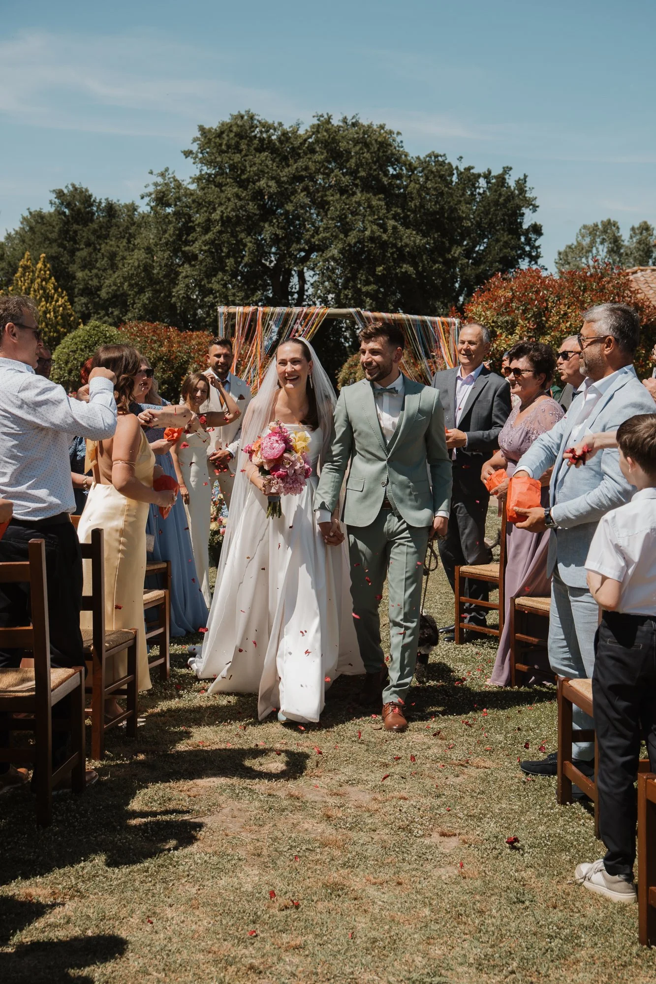 Ein Brautpaar beim Open-Air-Hochzeitsfest, das von Gästen umgeben ist.