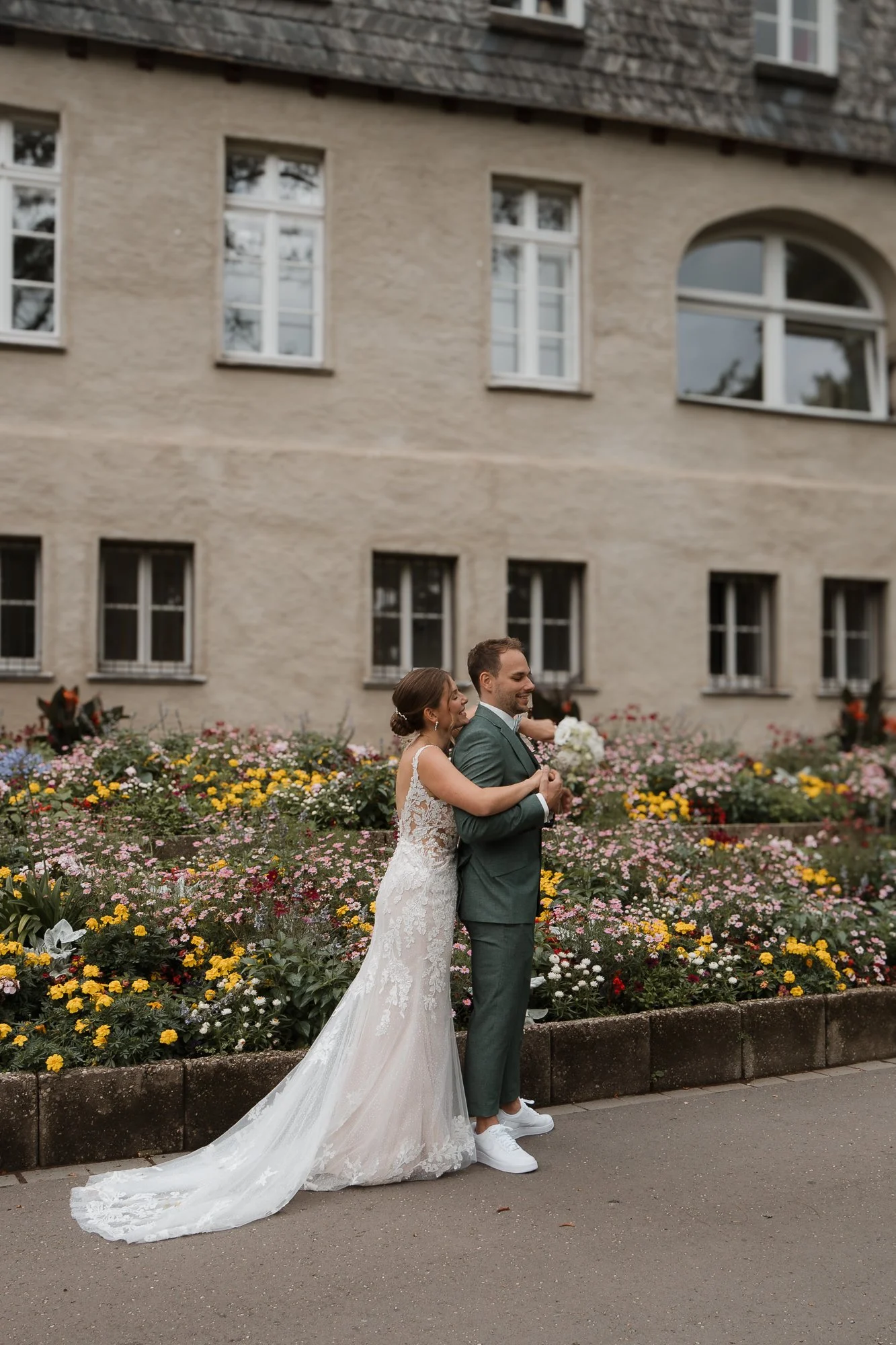 Ein brautpaar auf der Hochzeit tanzt vor einer Blumenrabatte vor einem alten Gebäude.