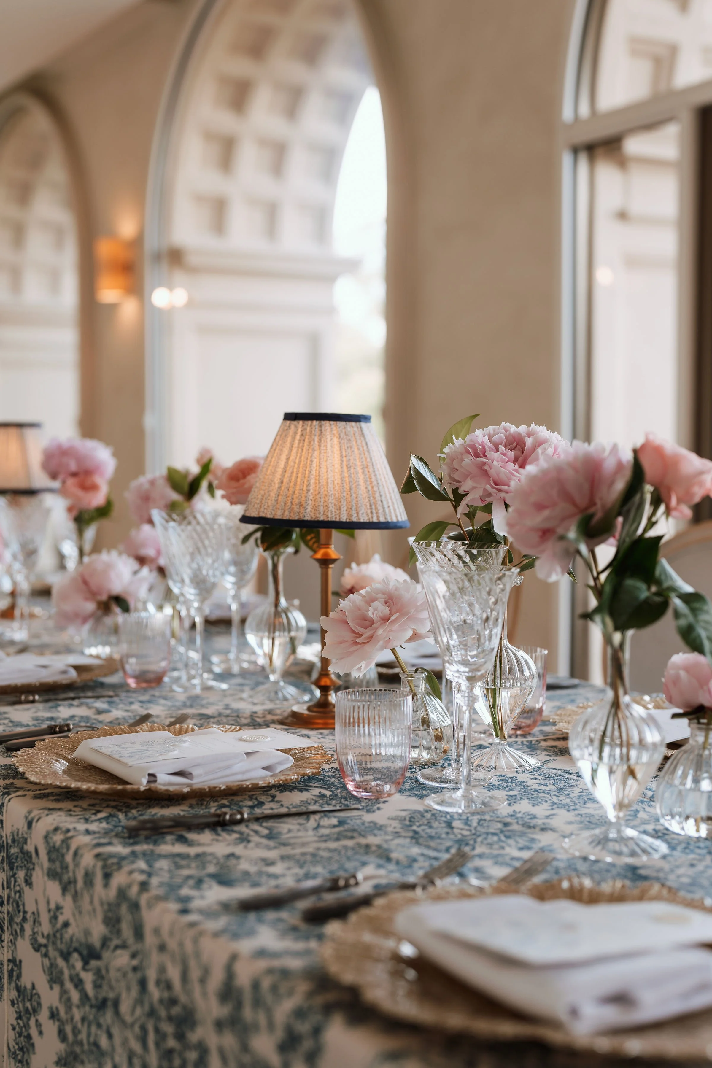 A table set for a buffet meal with plates of food, silverware, and glass plates, outside with greenery and water in the background.