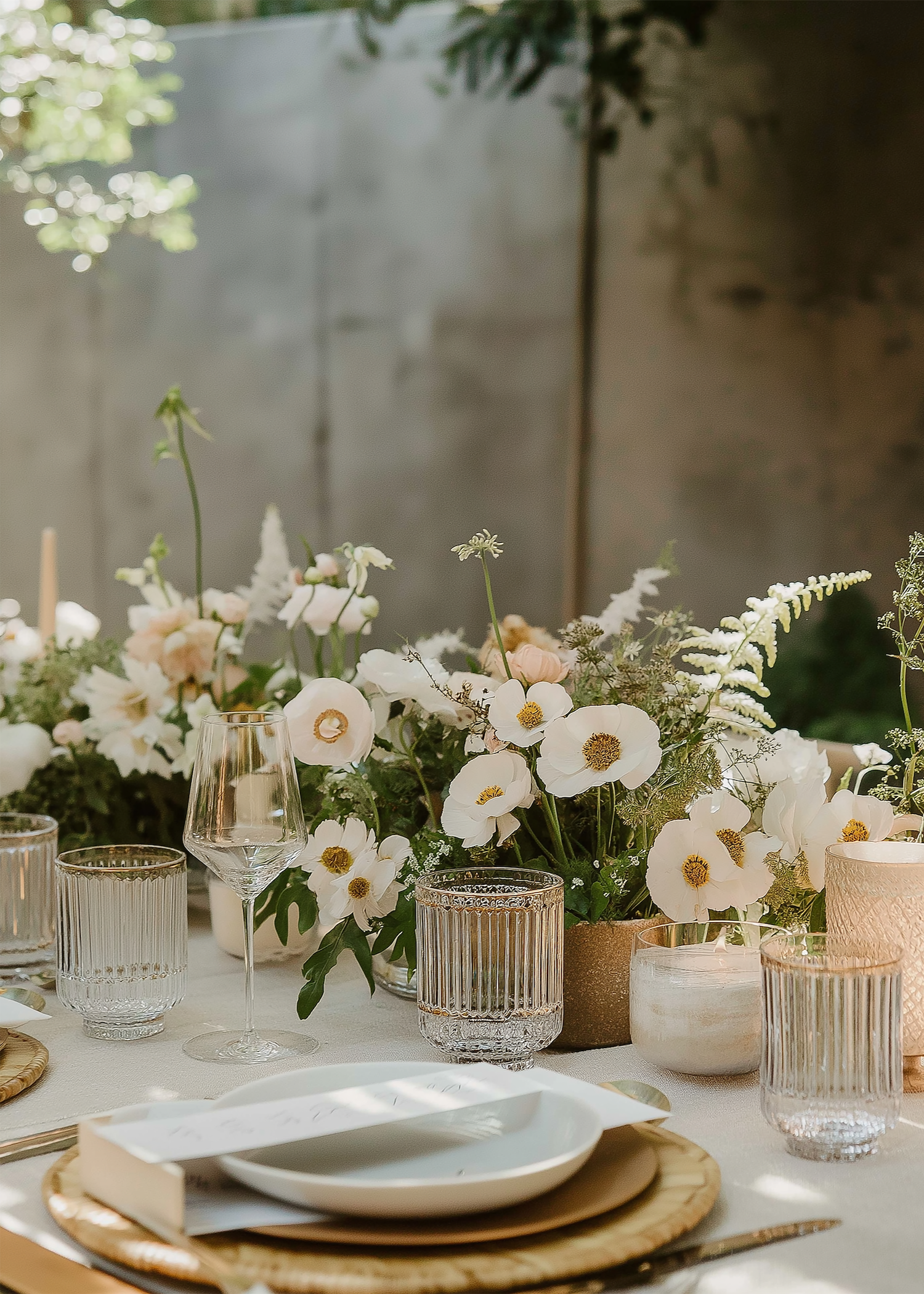 A table set for a buffet meal with plates of food, silverware, and glass plates, outside with greenery and water in the background.