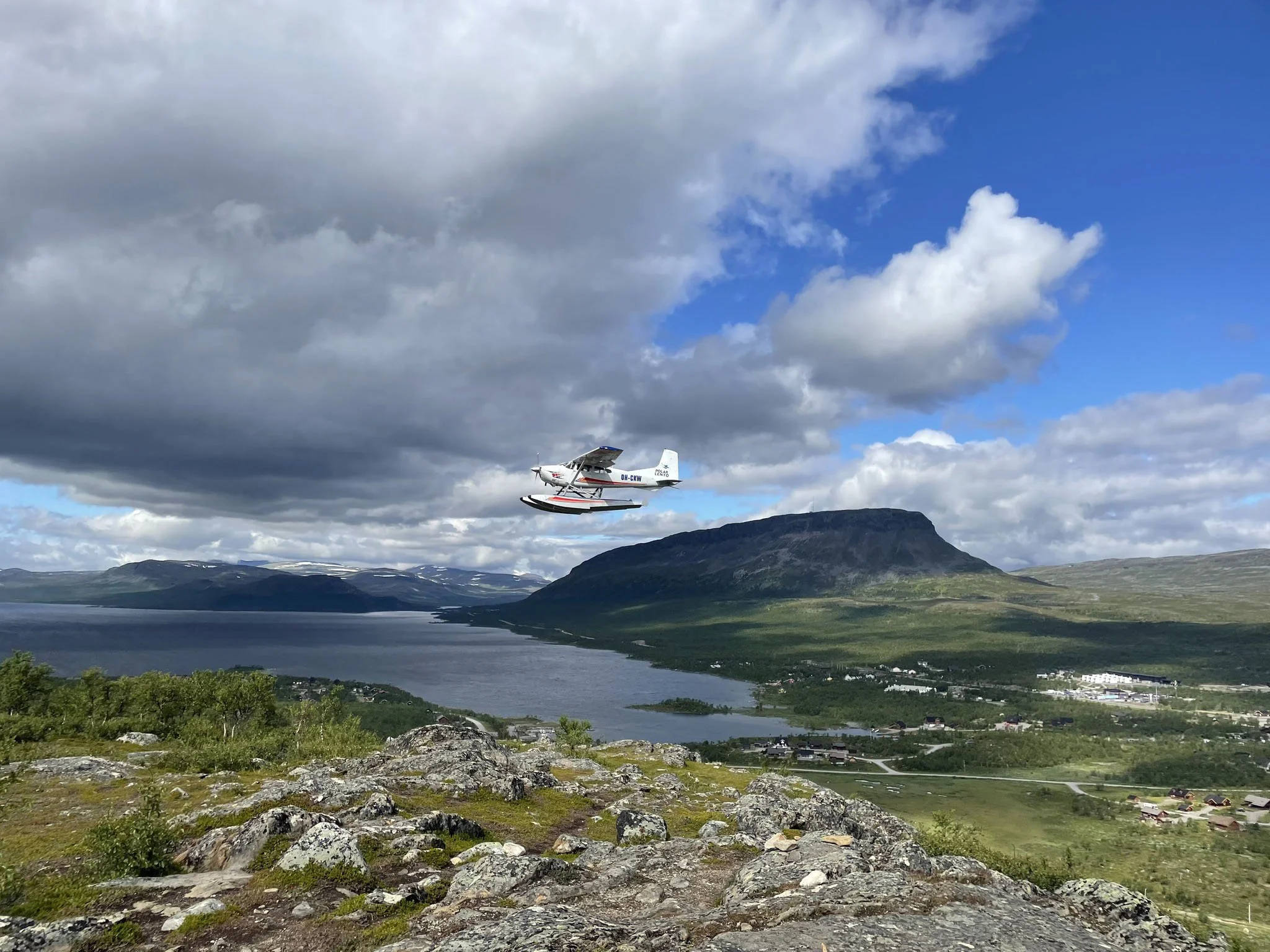 Polar-Lento Oy:n lentokone lentää tunturimaisemissa, taustalla pilviä ja järvi.