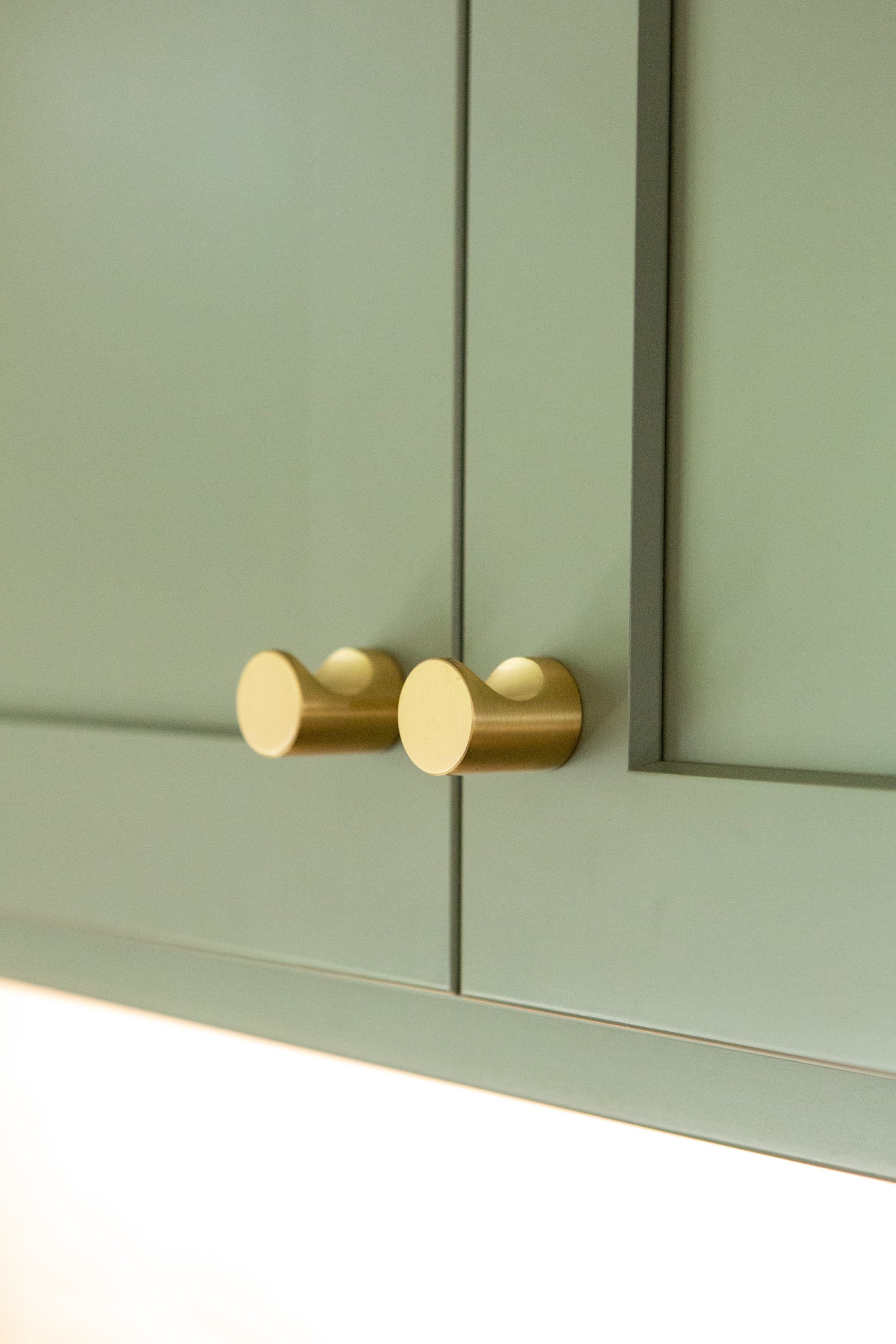 Close-up of light green cabinet door with cream-colored round knob handles.