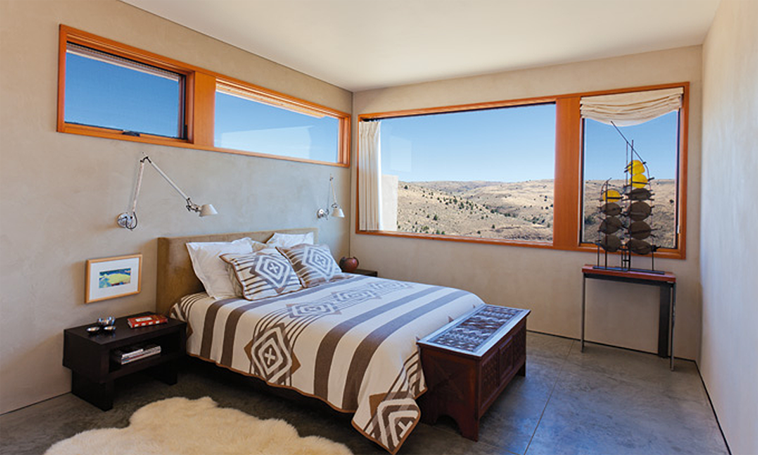 A bedroom with a bed, nightstand, and large windows showing a desert landscape.