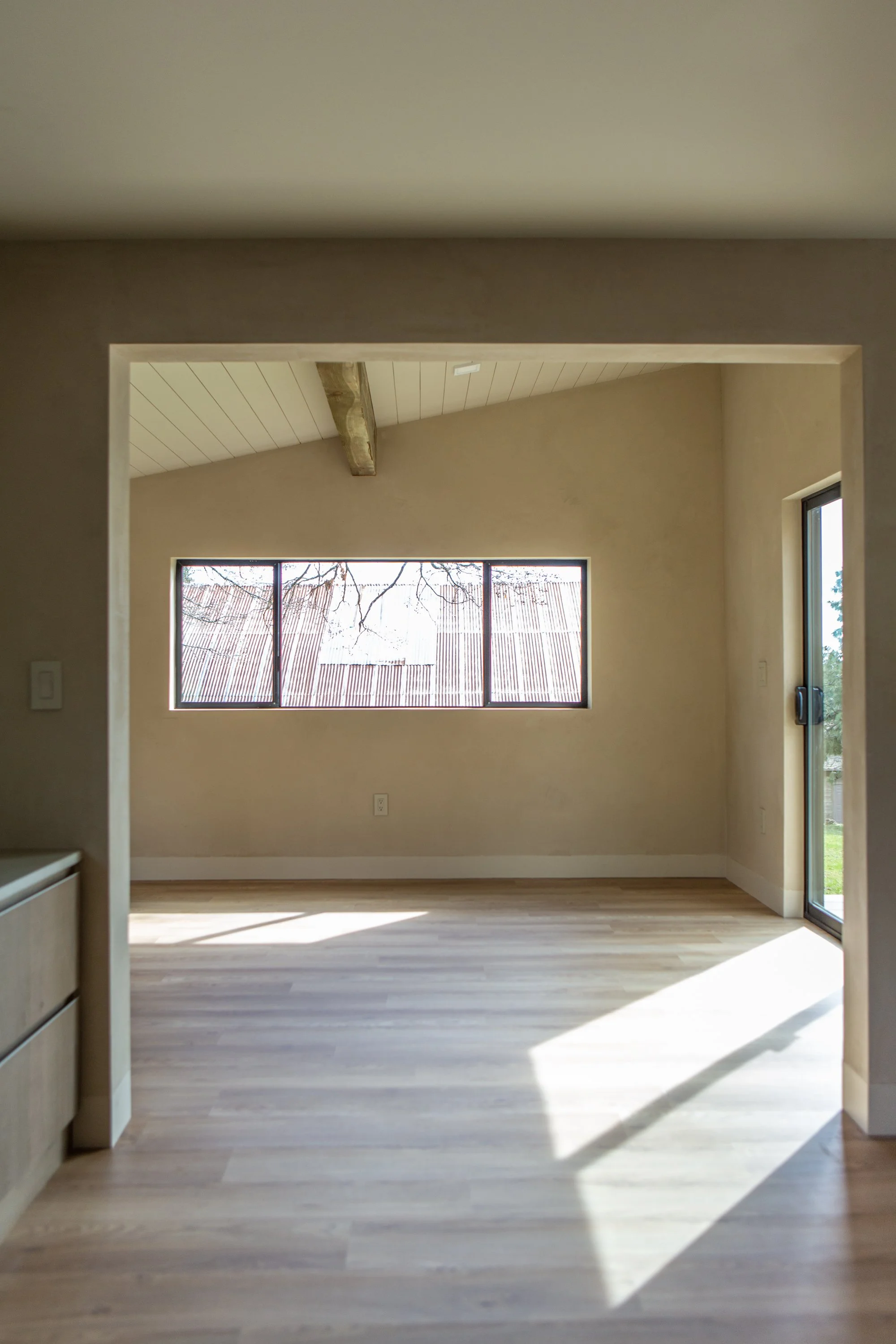 Empty room with large windows, light-colored wooden floors, and a partial view of a ceiling with exposed wooden beams.