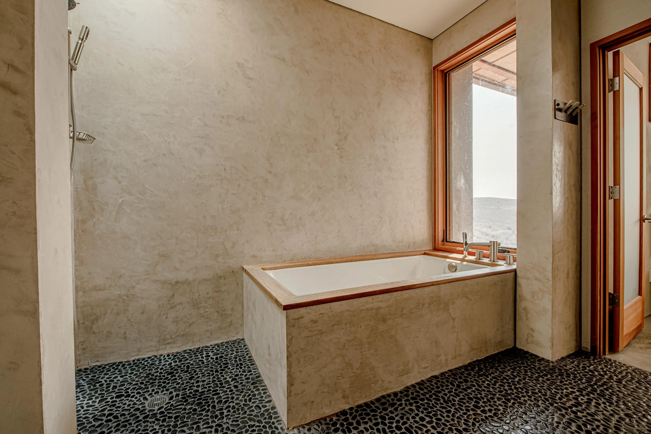 Bathroom with a built-in bathtub next to a large window, a showerhead on the wall, and patterned black and white floor tiles.