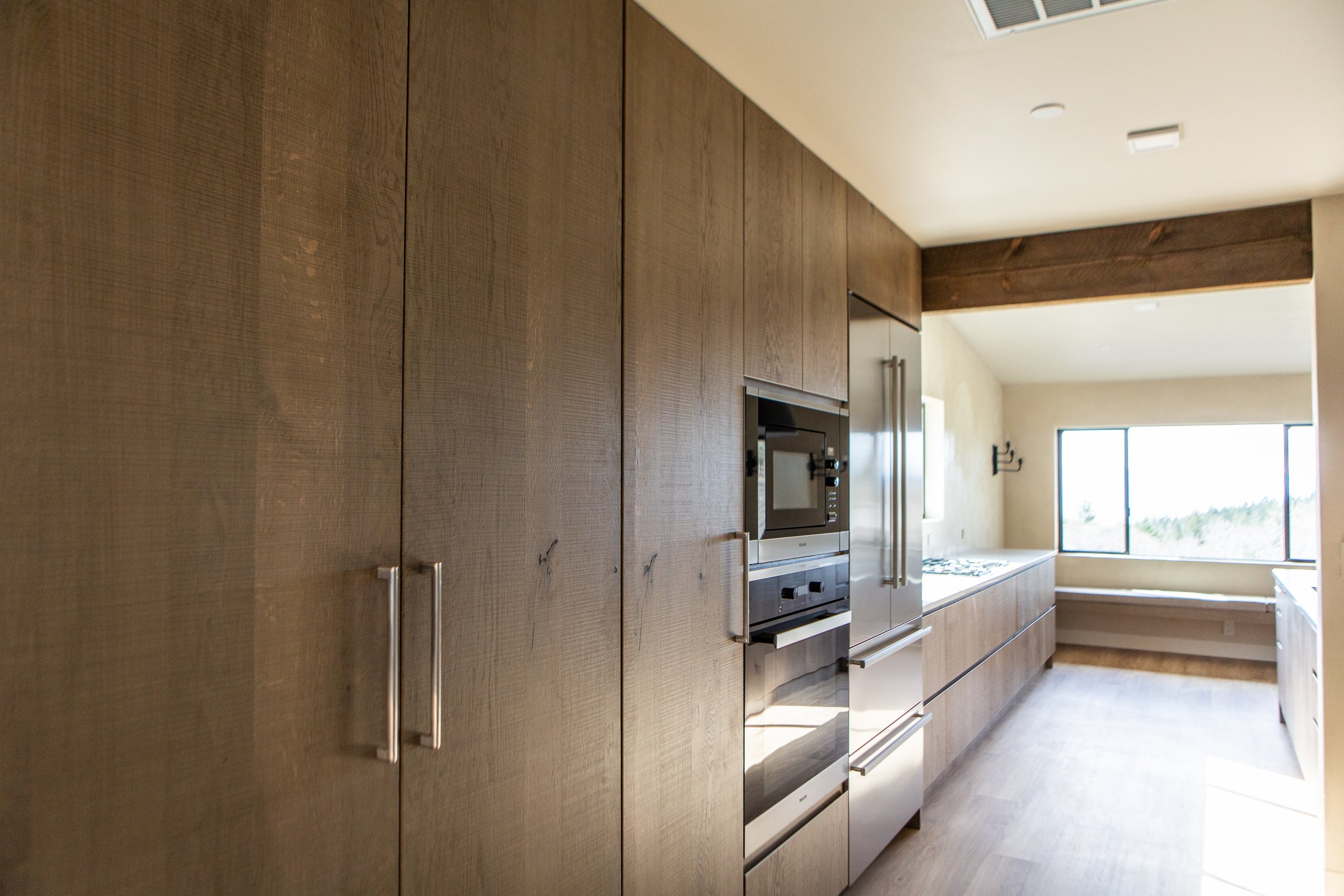 Modern kitchen with wooden cabinetry and built-in stainless steel appliances, large window, and beige walls.