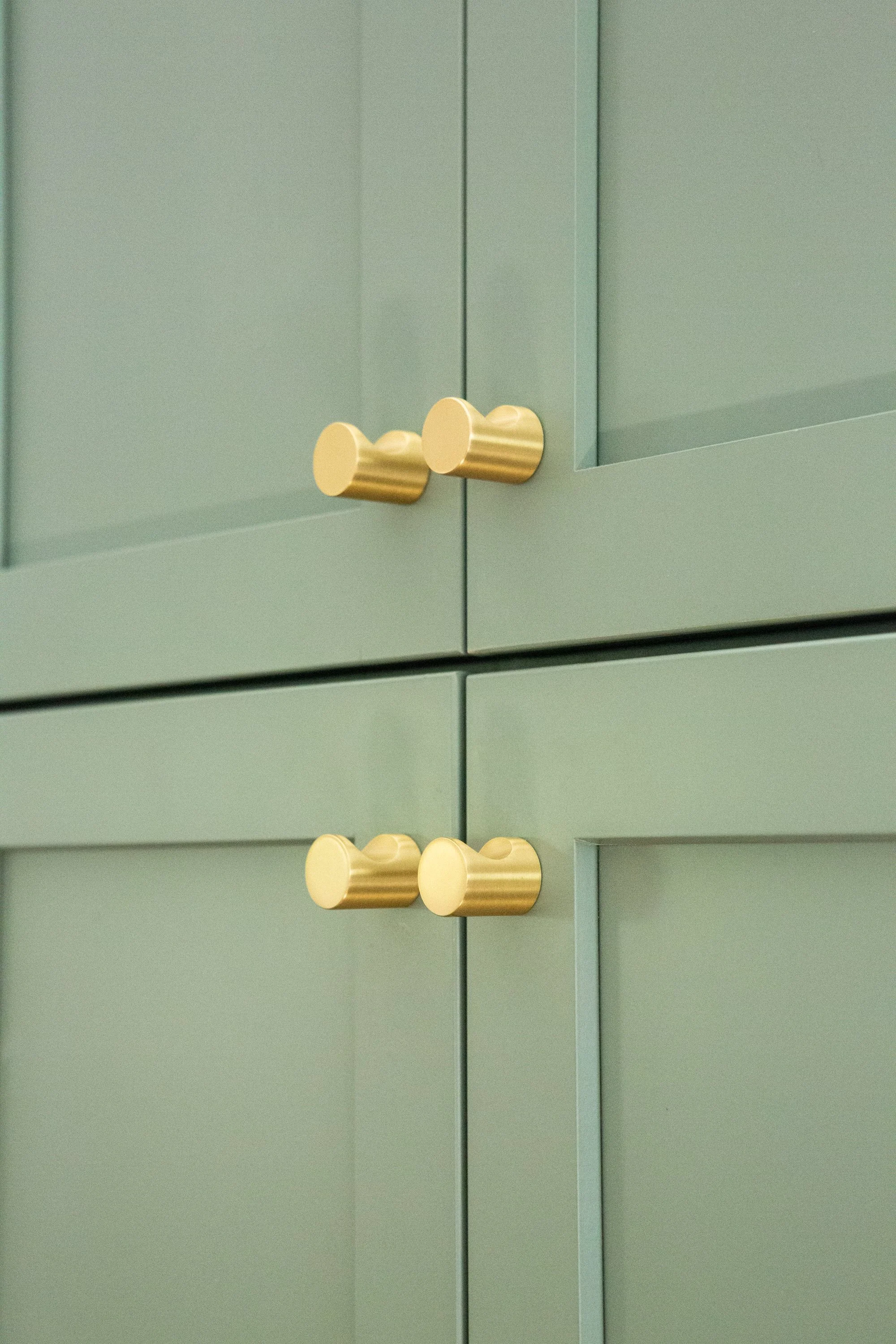 Close-up of a mint green cabinet with three gold knobs on the door.