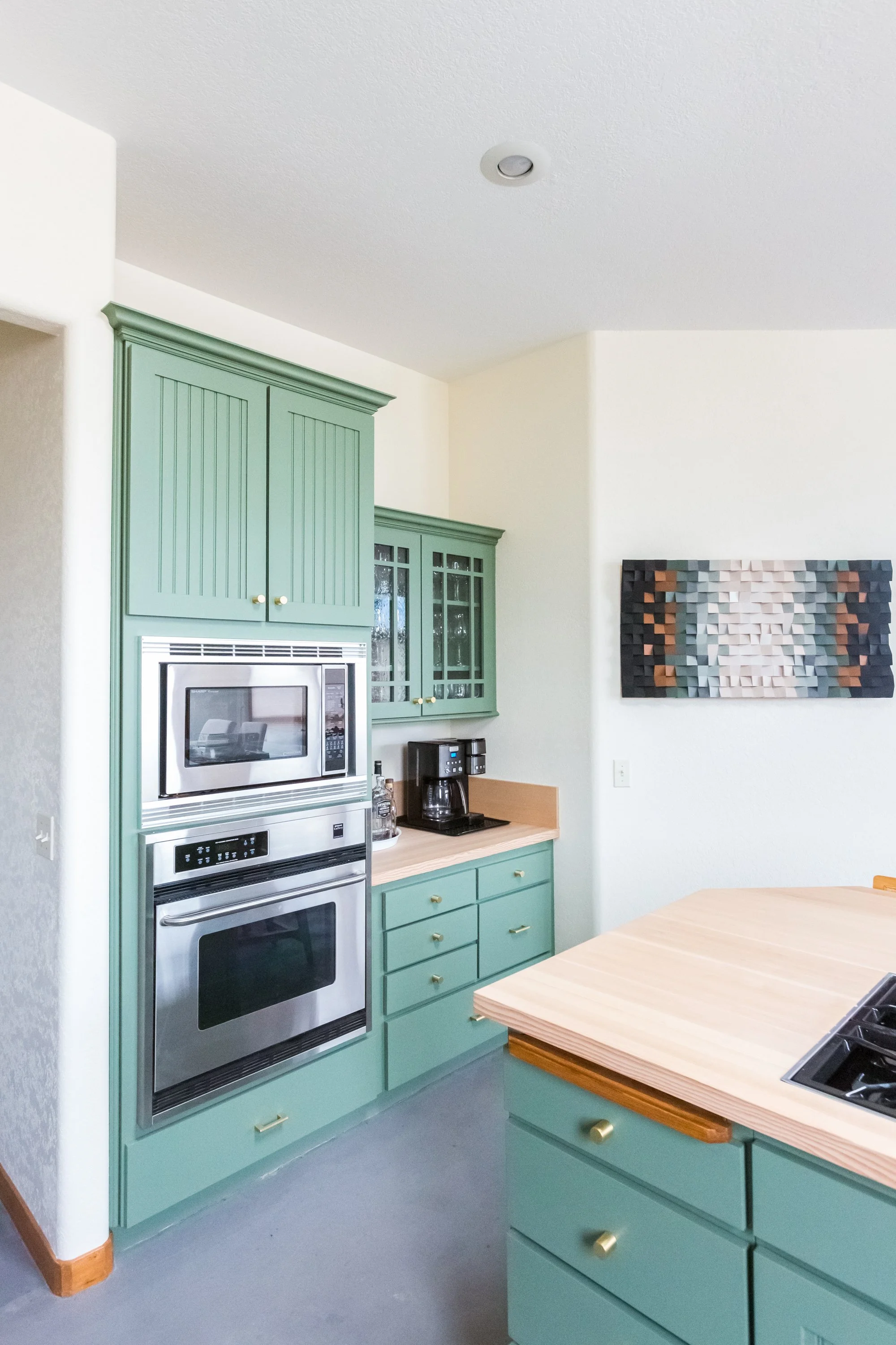Kitchen with mint green cabinets, a stainless steel microwave oven, a window, and a colorful abstract wall art.