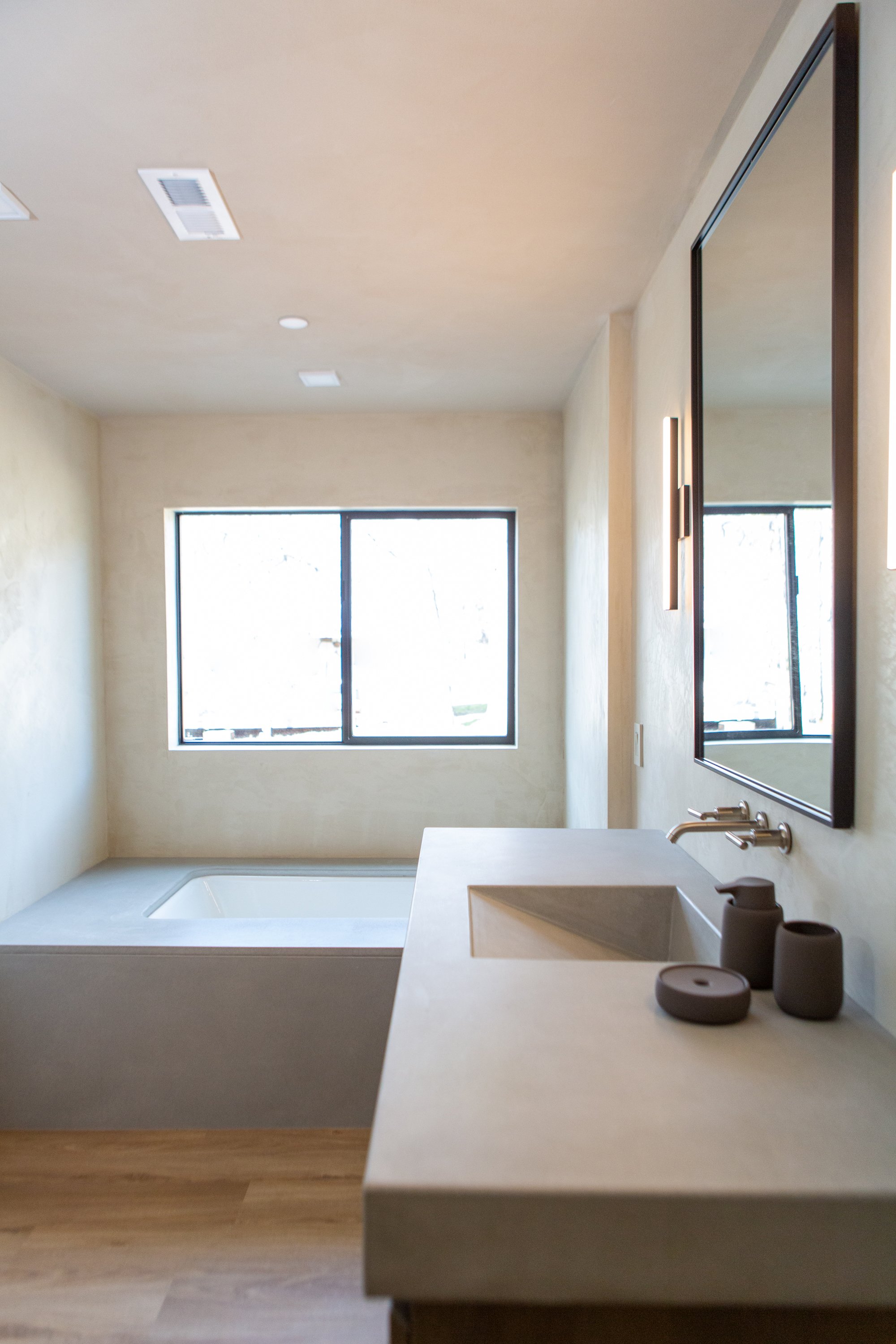 Modern bathroom with a large window, a built-in bathtub, a sink with a countertop, and a mirror on the wall.