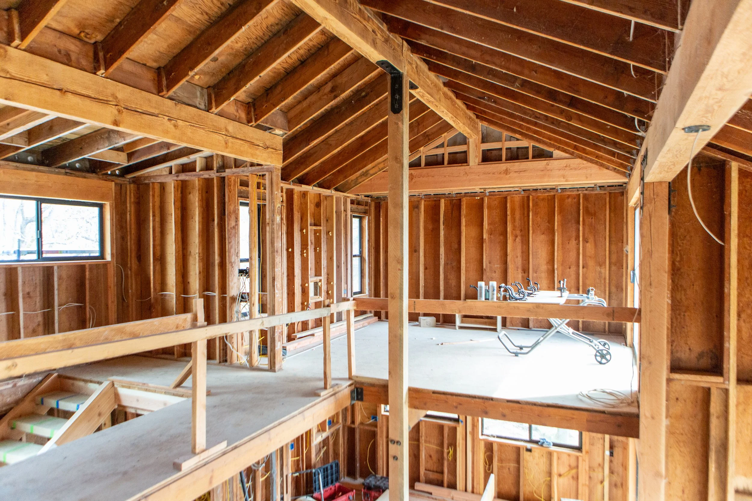 Interior of a house under construction, showing wooden framing, some electrical wiring, windows, and a concrete floor.
