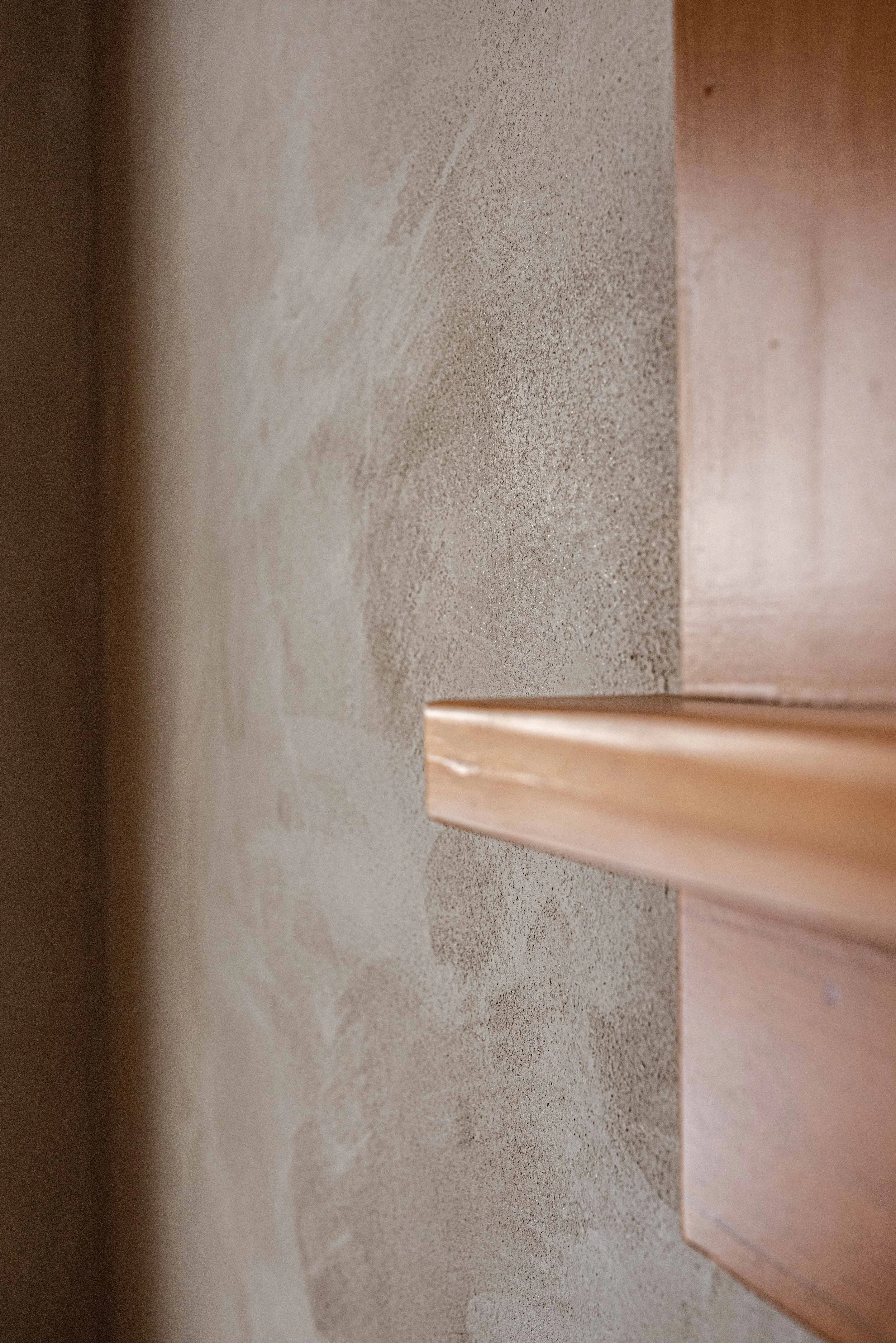 Close-up of a wooden piece on a textured beige wall