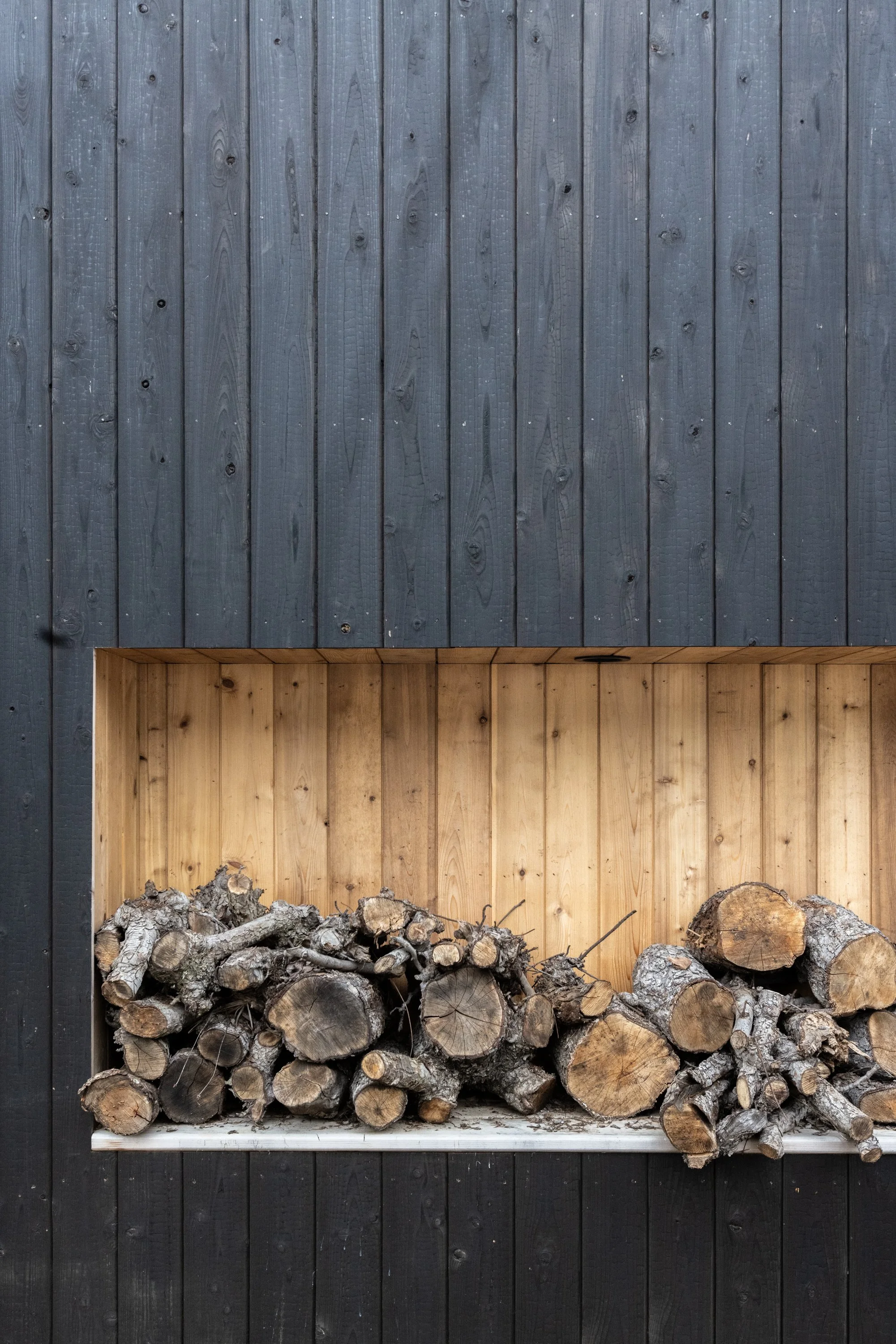 Stacked firewood placed inside a wooden frame against a dark wooden wall.