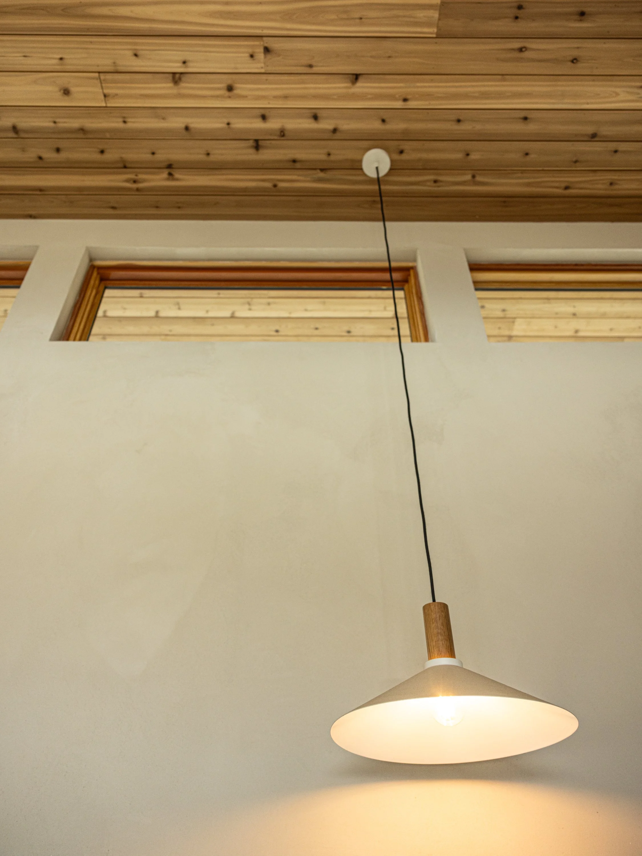Interior ceiling with wooden paneling, a hallway window, and a hanging light fixture with a white and beige shade.