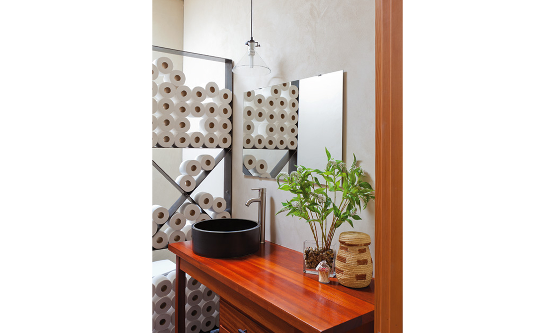 Bathroom vanity with a black vessel sink, a tall green plant, a woven container, and a small decorative object, with a mirror and decorative wall panels behind.
