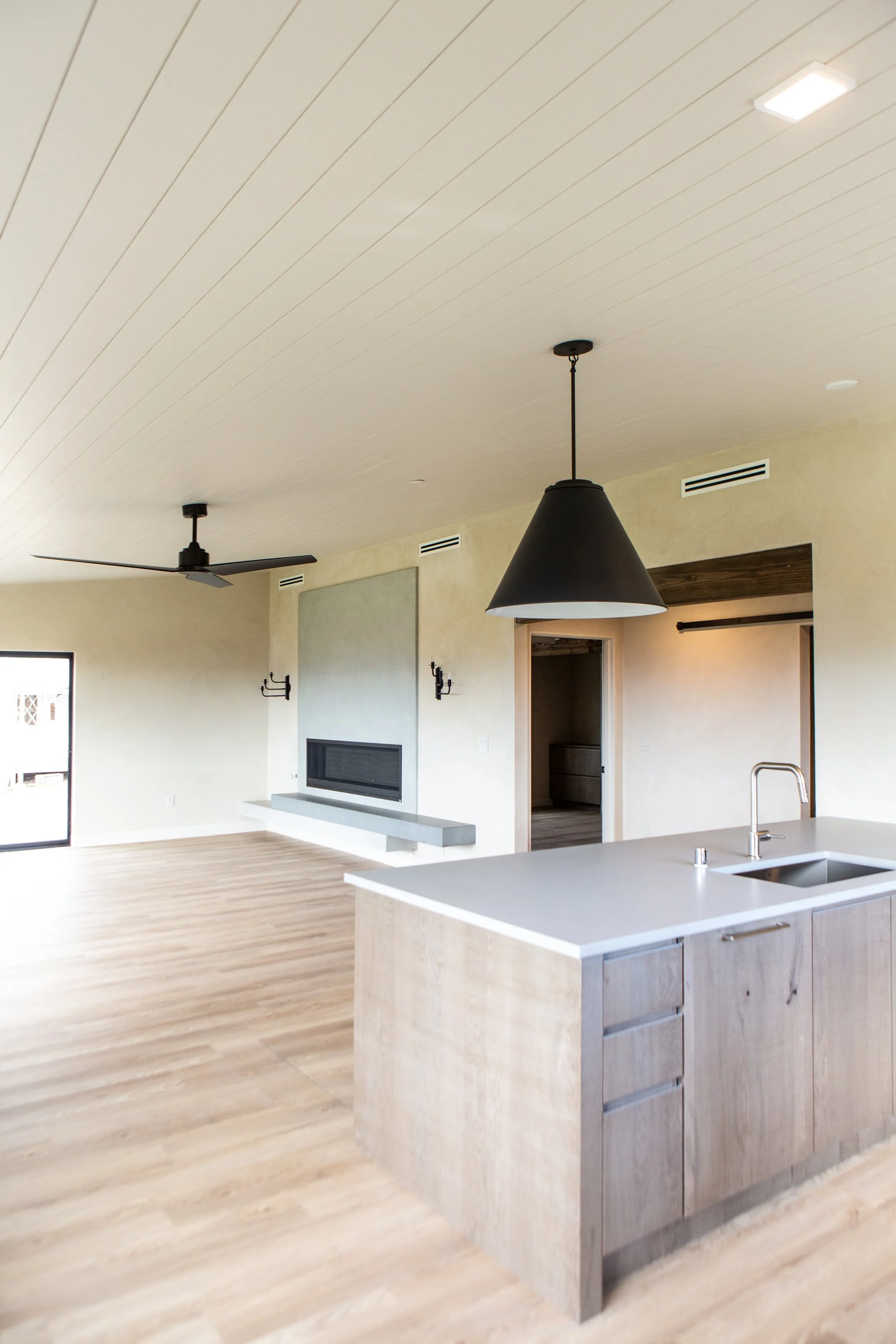 Modern open-concept kitchen with island, pendant lighting, ceiling fan, and fireplace in living area.