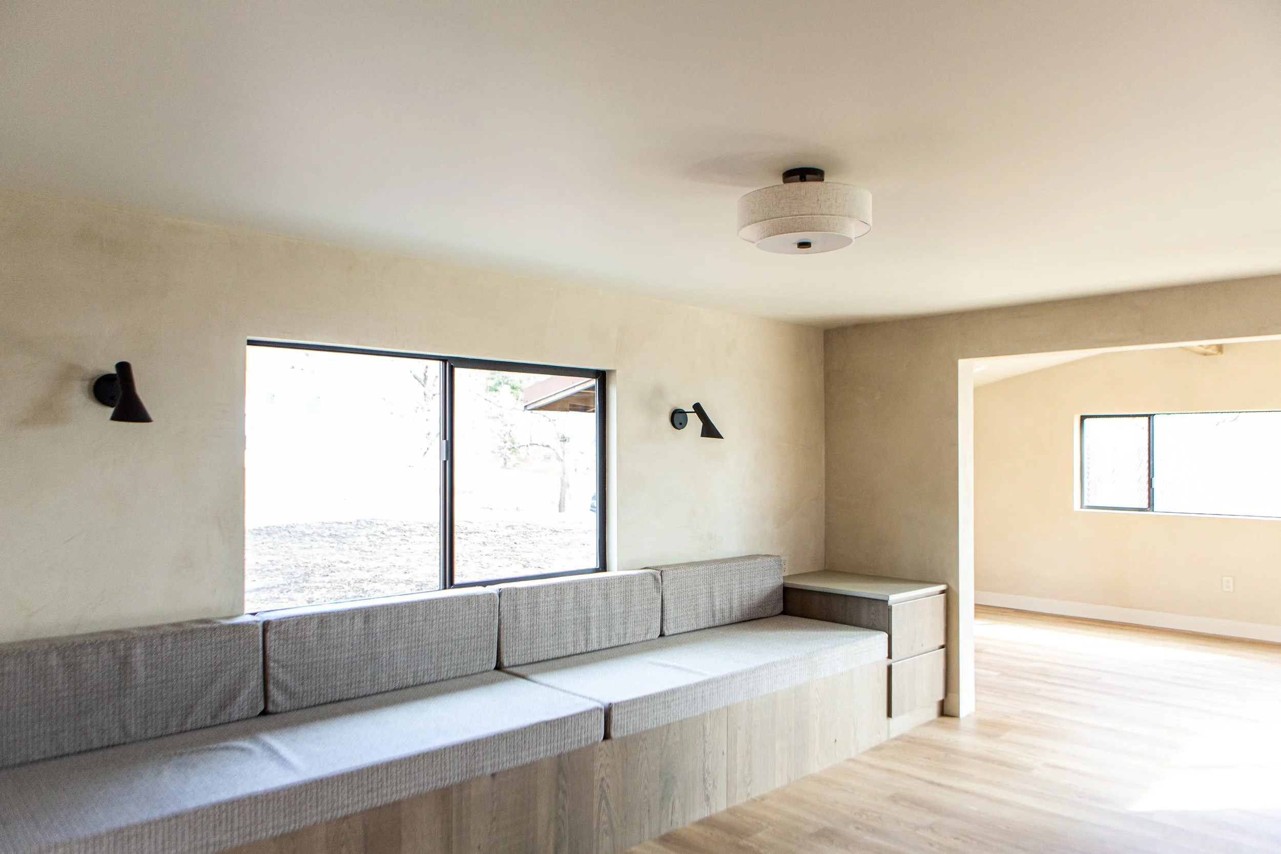 Living room with beige built-in sofa, large window, and wooden floor.