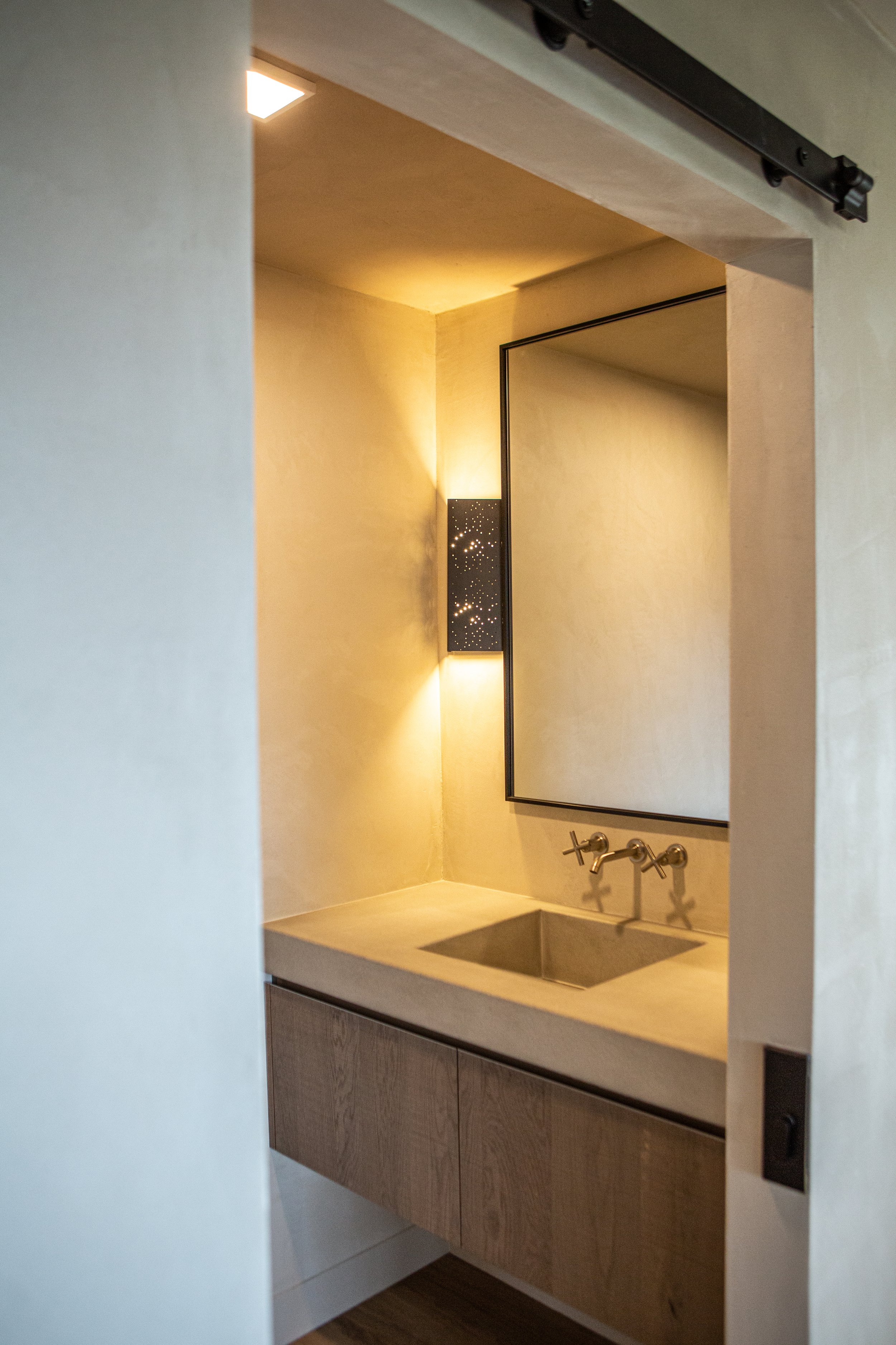 A modern bathroom with a mirror, a sink with wall-mounted faucet, and wooden cabinetry.