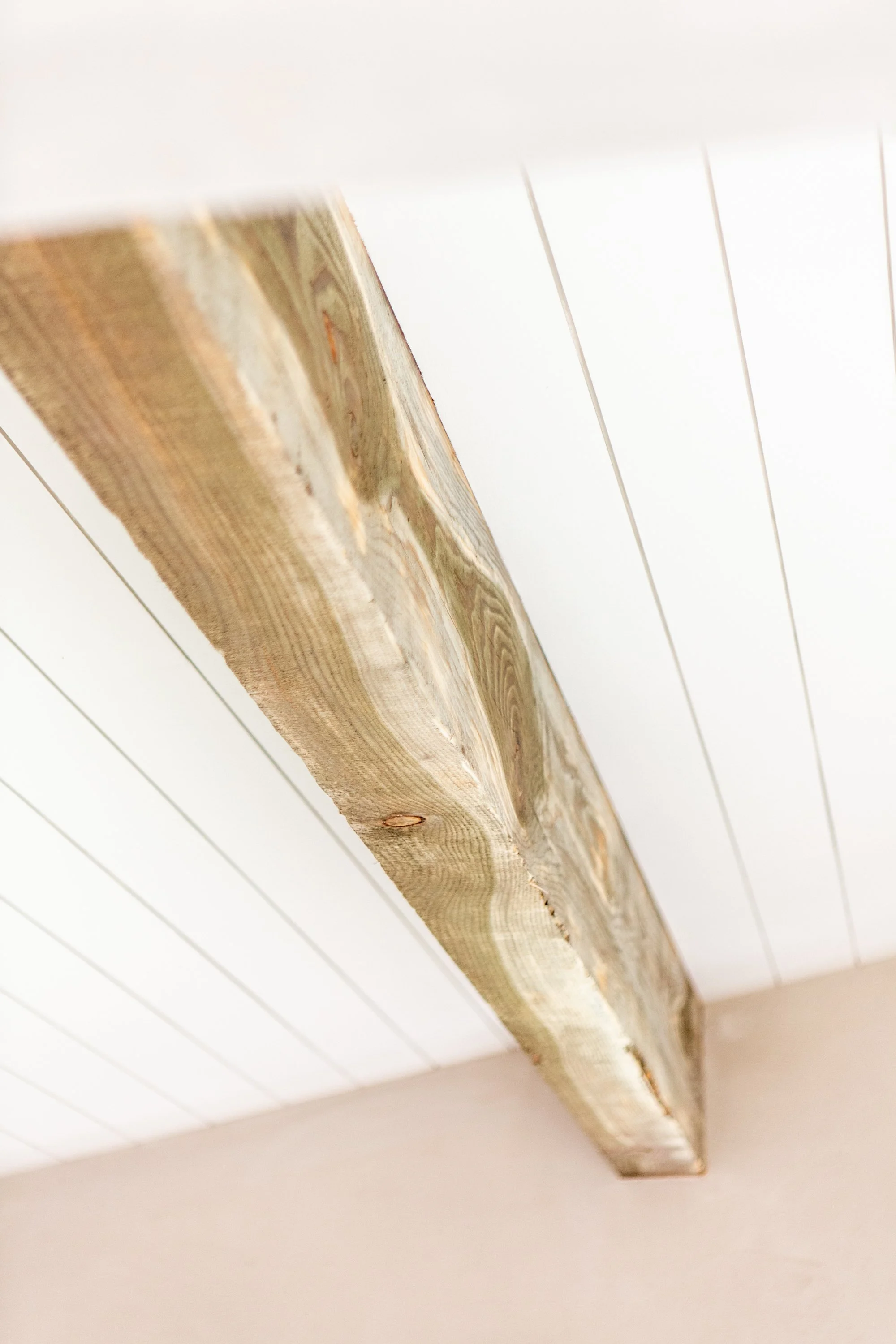 A close-up view of a wooden beam mounted on a white ceiling with horizontal wooden slats.