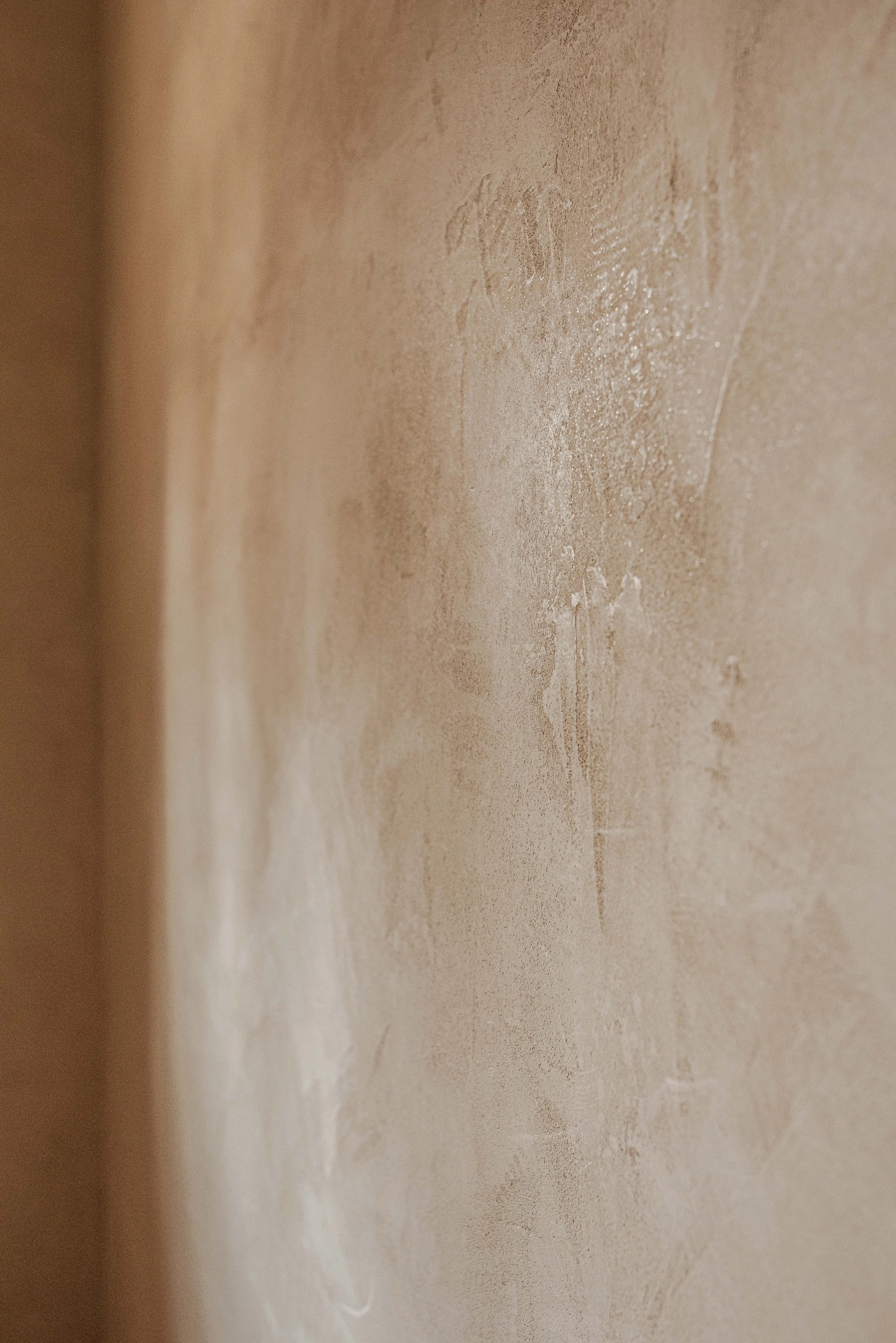 Close-up of beige textured wall with faint markings and a corner shadow.
