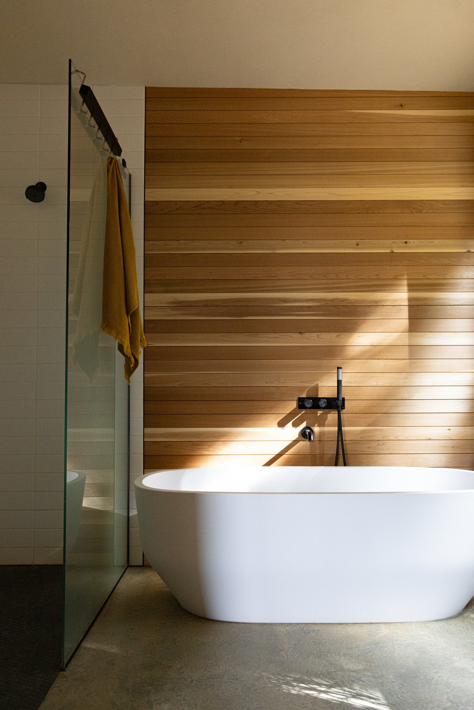 Modern bathroom with a freestanding bathtub, wooden wall paneling, and a walk-in shower with a glass partition and yellow towel.