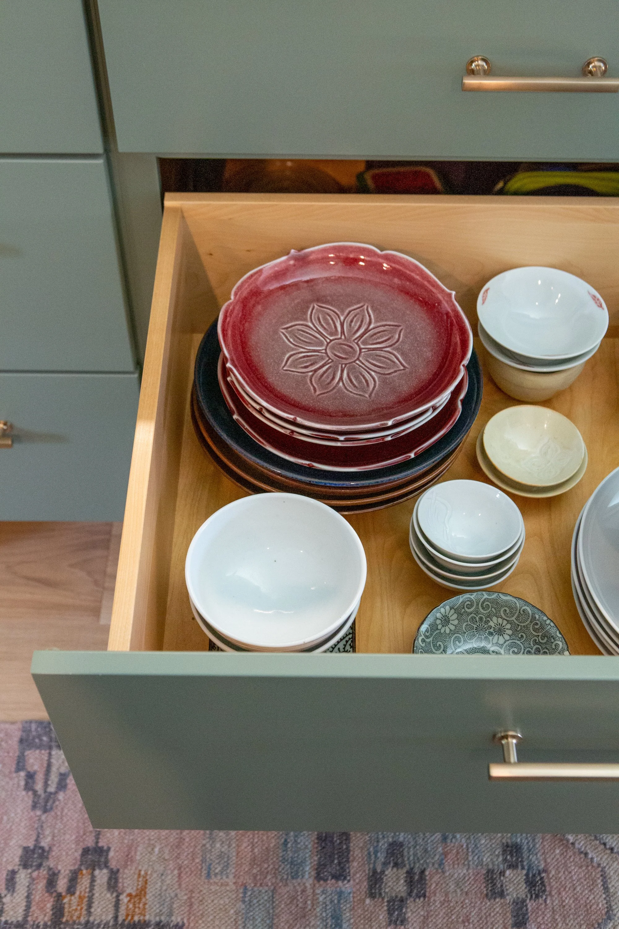 Open drawer with stacked ceramic plates in various colors and patterns.