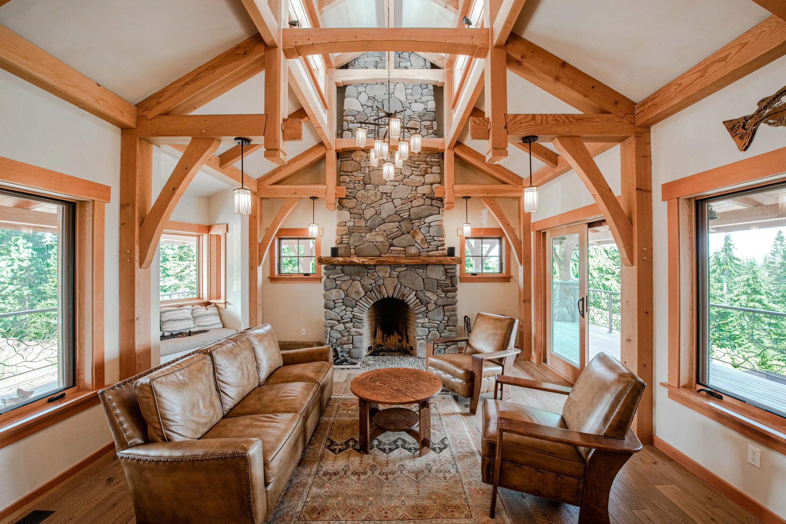 Living room with leather sofas, wooden coffee table, stone fireplace, large windows, and chandelier hanging from the ceiling.