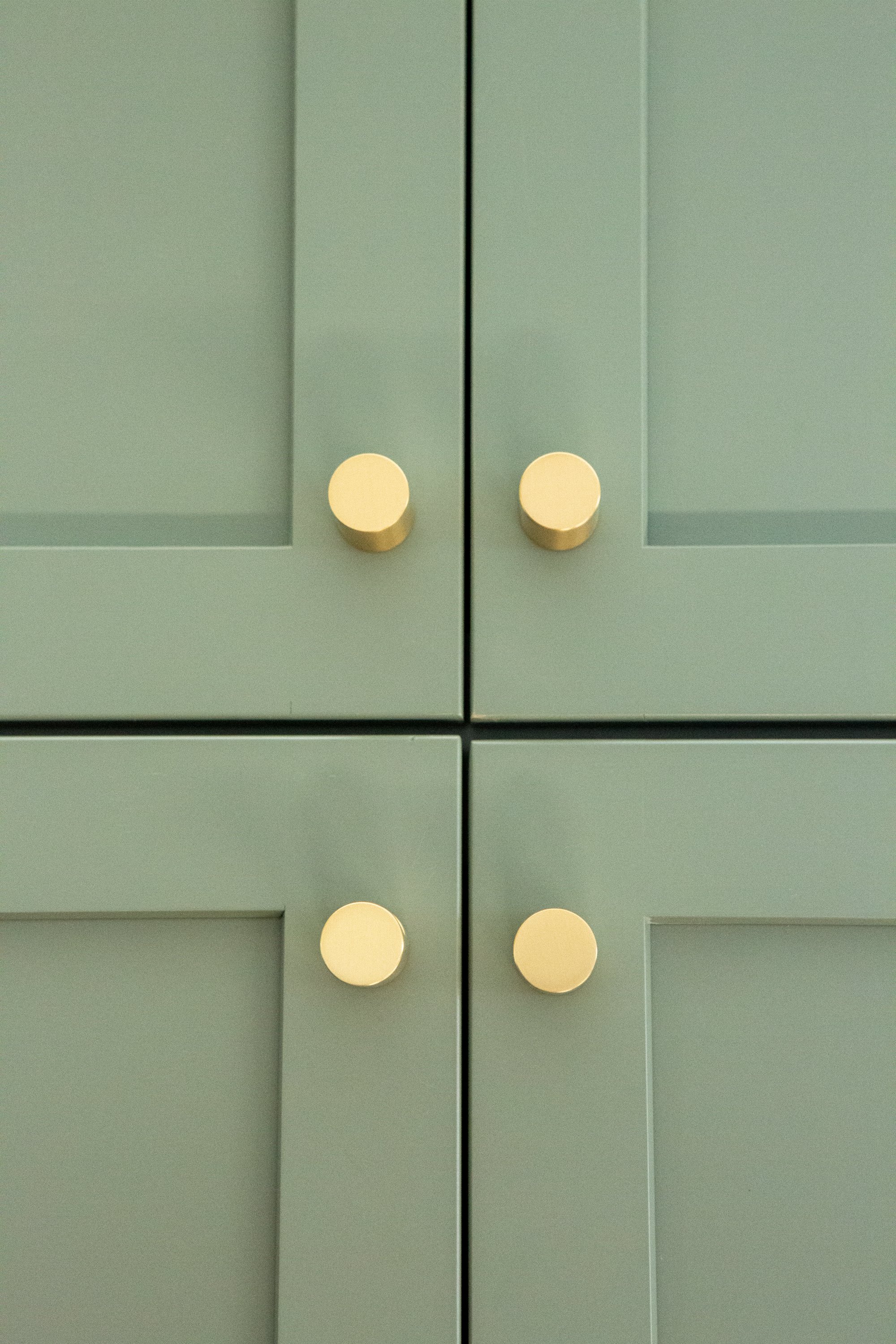 Close-up of green cabinet doors with round, beige knobs.