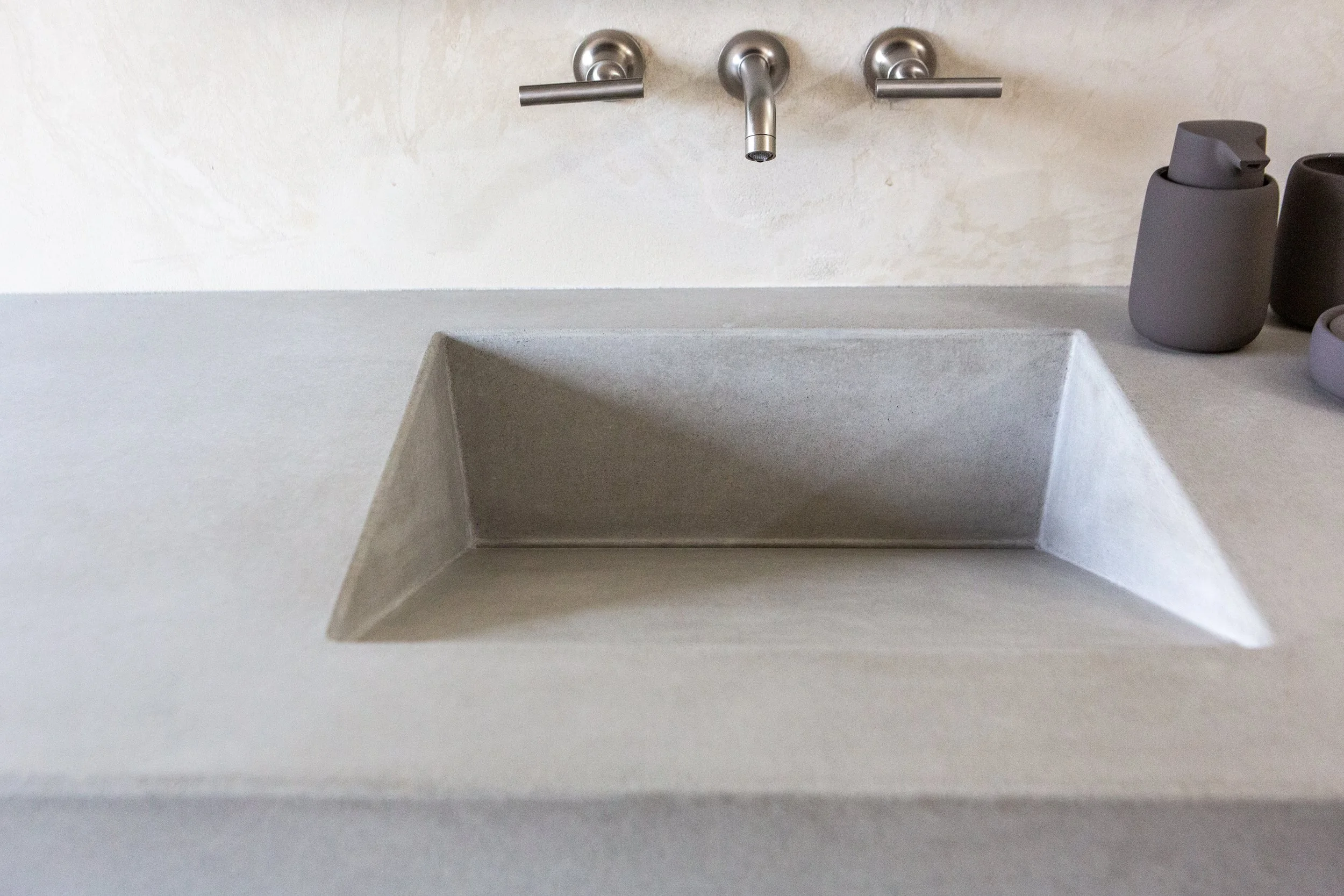 A modern kitchen sink with a metallic faucet, gray soap dispenser, and a gray container on a light-colored countertop.