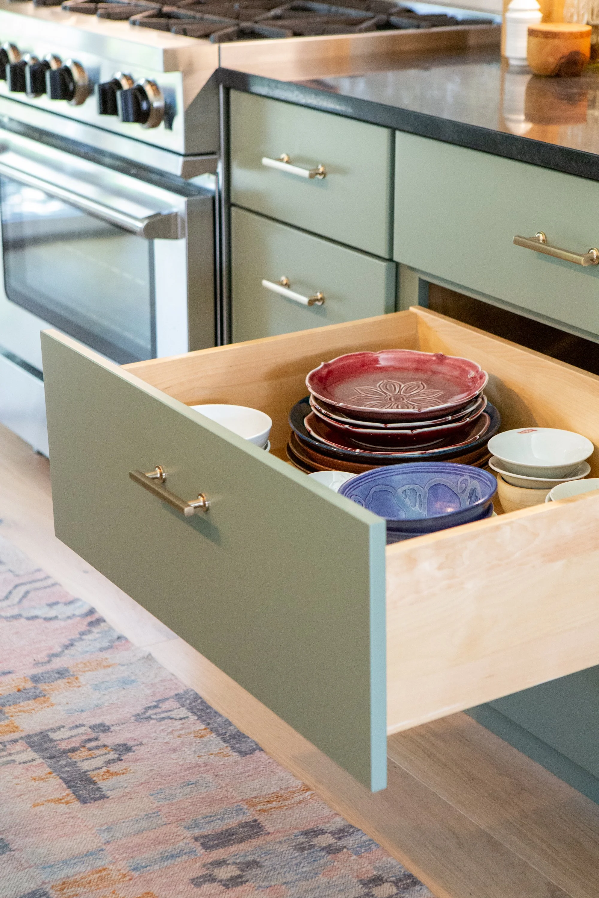 Open kitchen drawer filled with stacked ceramic plates in red, blue, and white.