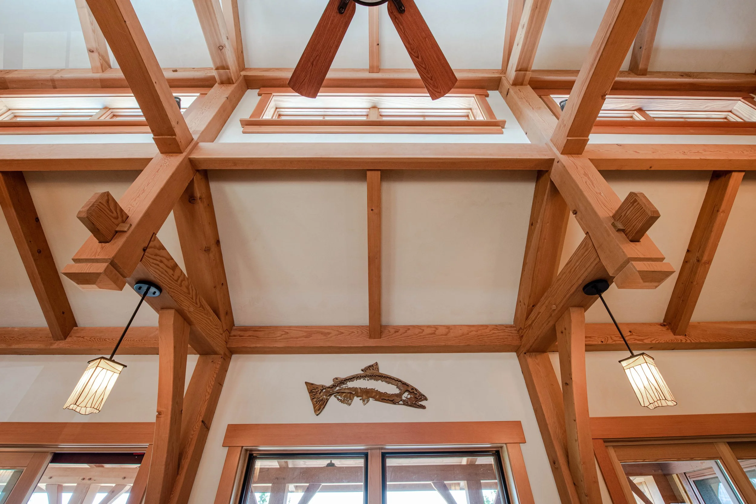 Interior view of a ceiling with wooden beams, mounted lamps, and a decorative wall hanging shaped like a fish.