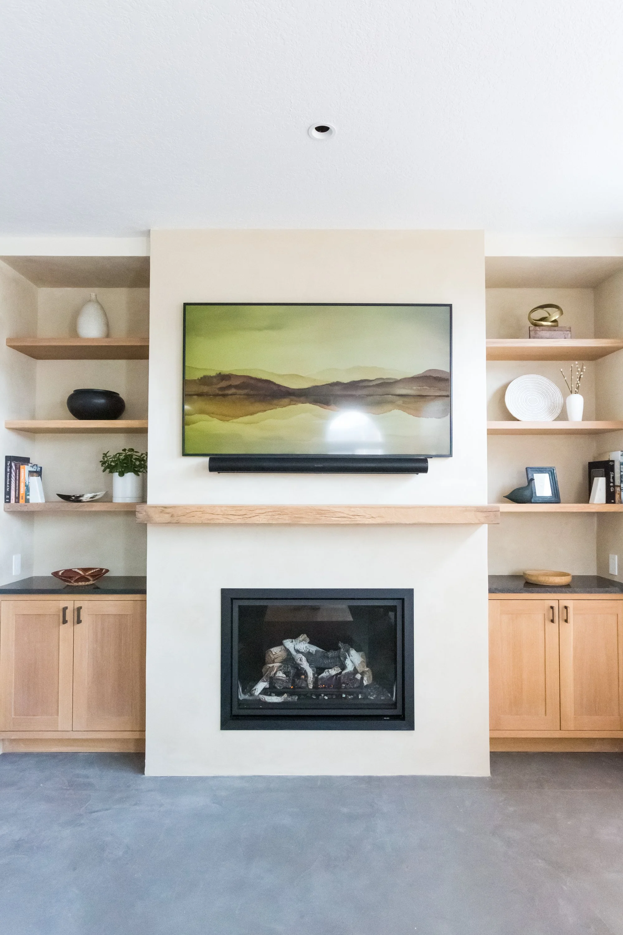 Living room with a fireplace, a painting of a lake and mountains, and wooden shelves with decorative items.