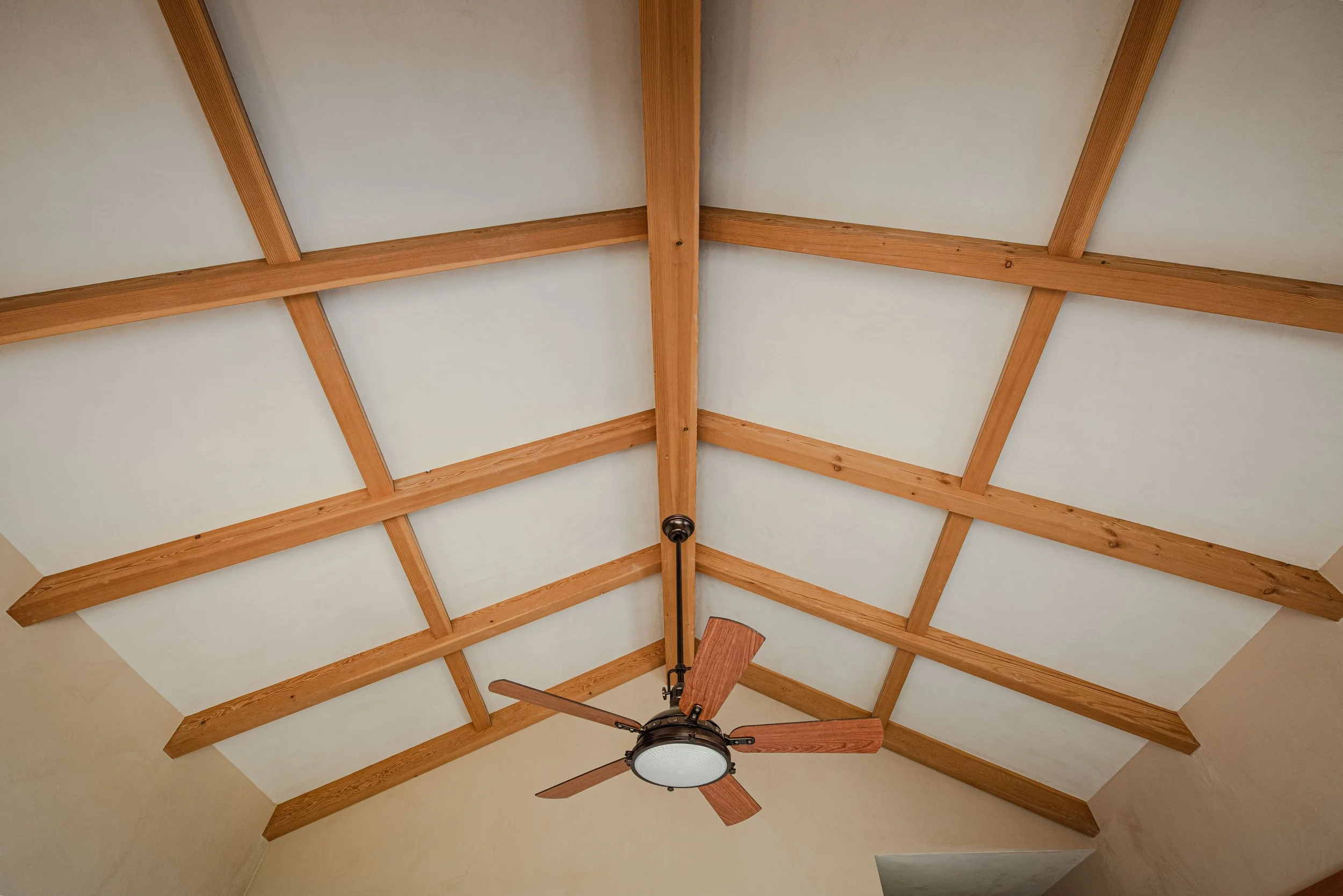 Ceiling with wooden beams and a ceiling fan with dark blades and a light fixture in the center.