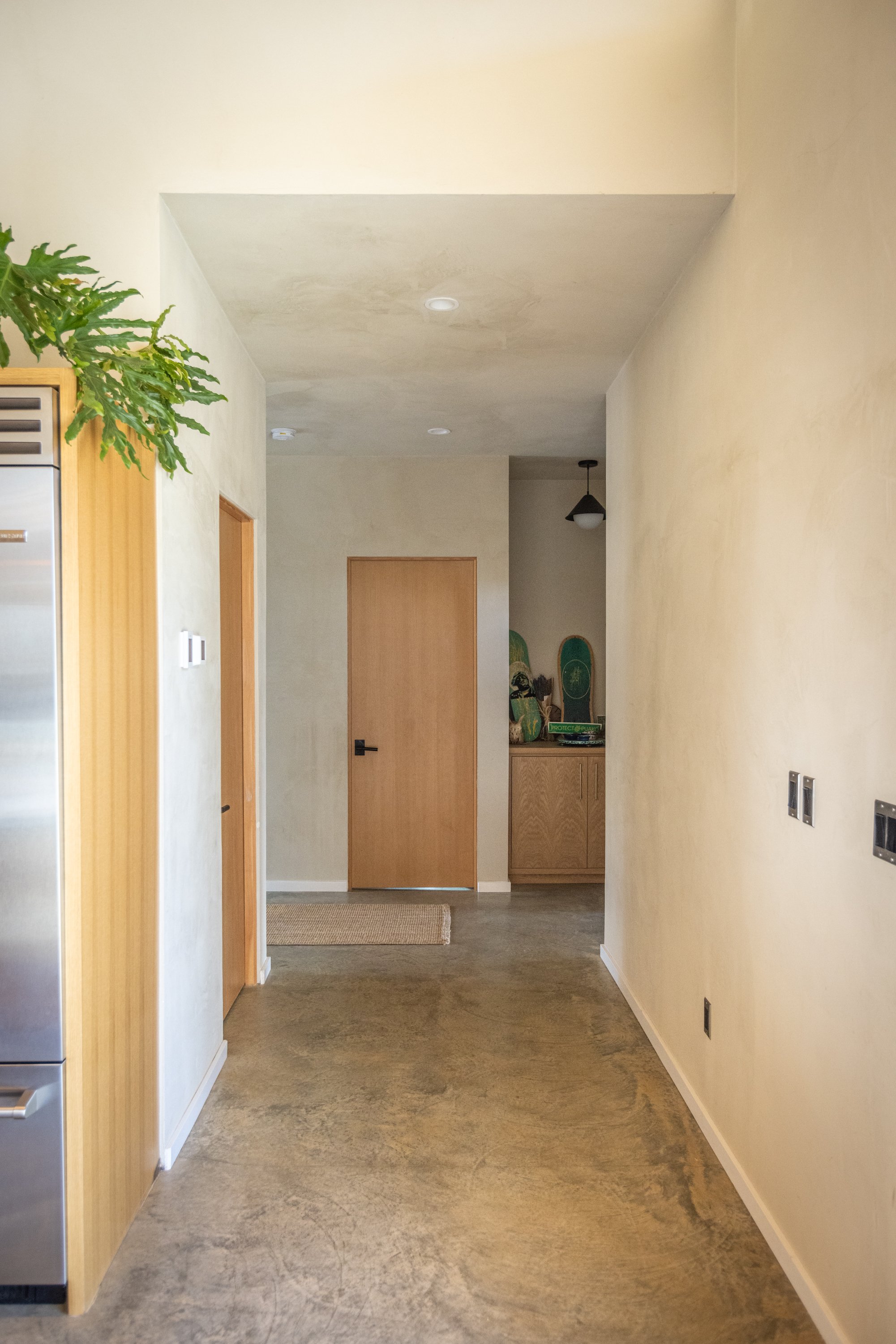A hallway with neutral-colored walls, wooden doors, a small wooden cabinet, and skateboard decks on top, with a light fixture on the ceiling.