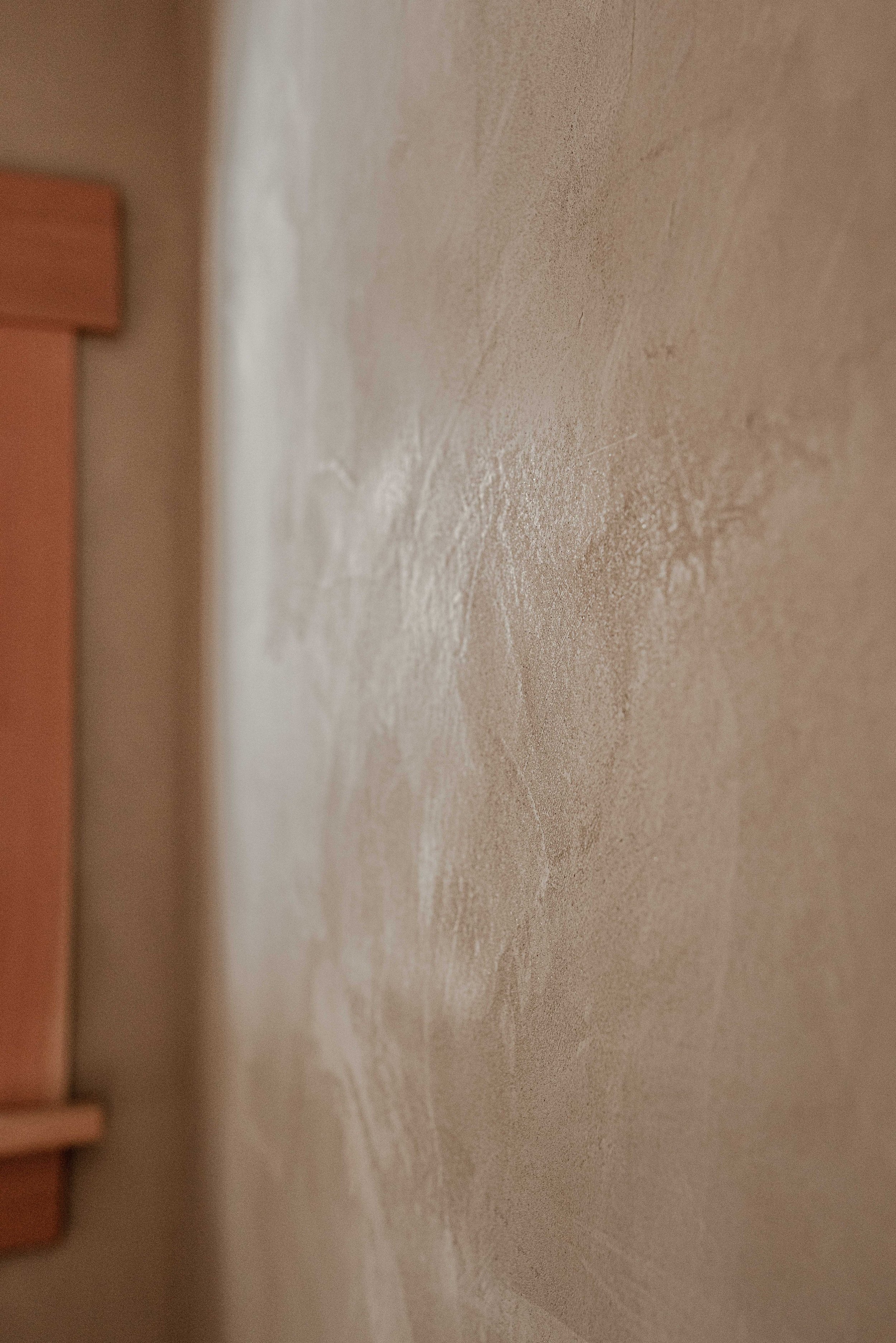 Close-up of a beige textured wall with a corner and part of a wooden surface in the background.