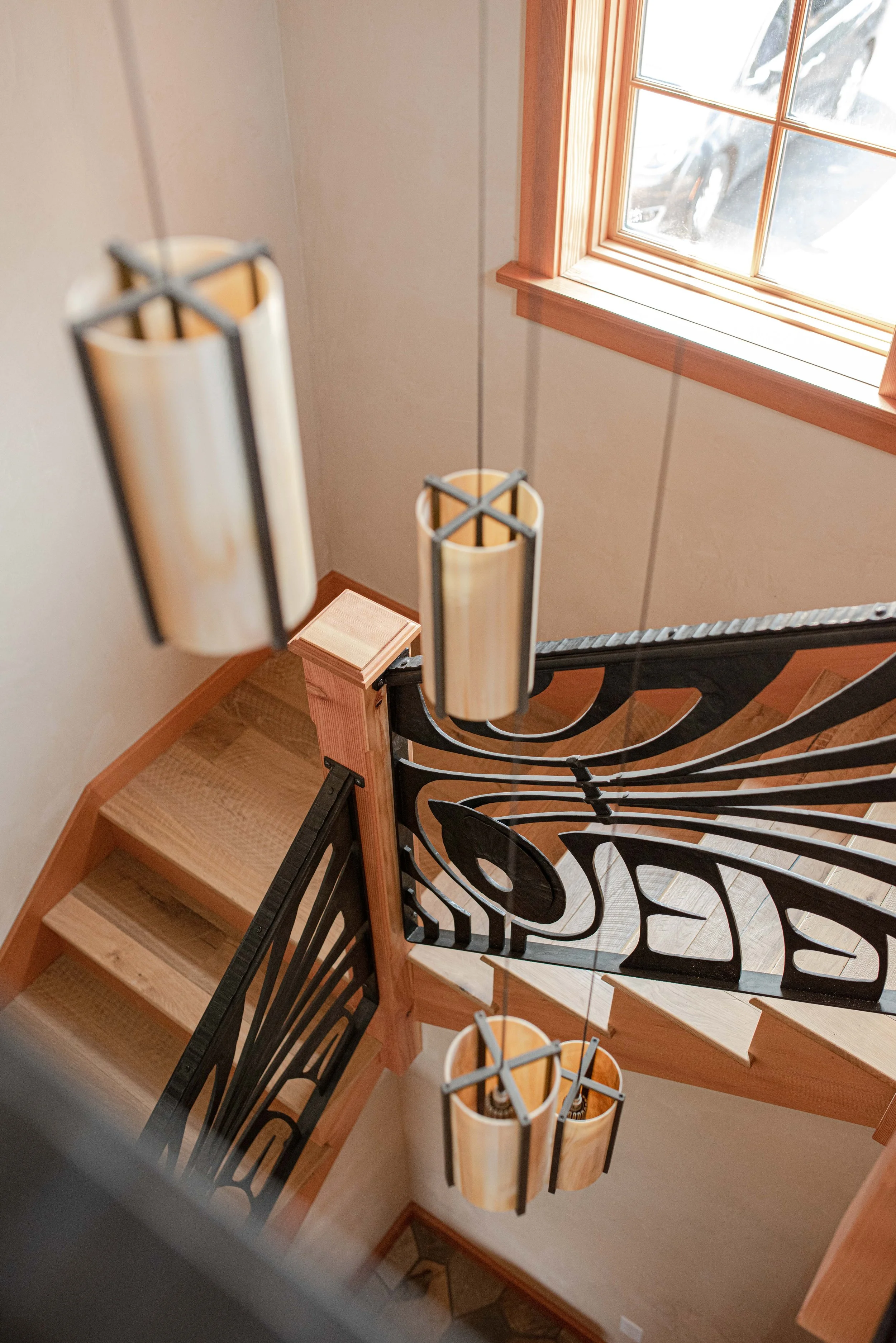 Wooden staircase with iron railing, hanging bamboo light fixtures, and a window with wooden trim near the stairs.
