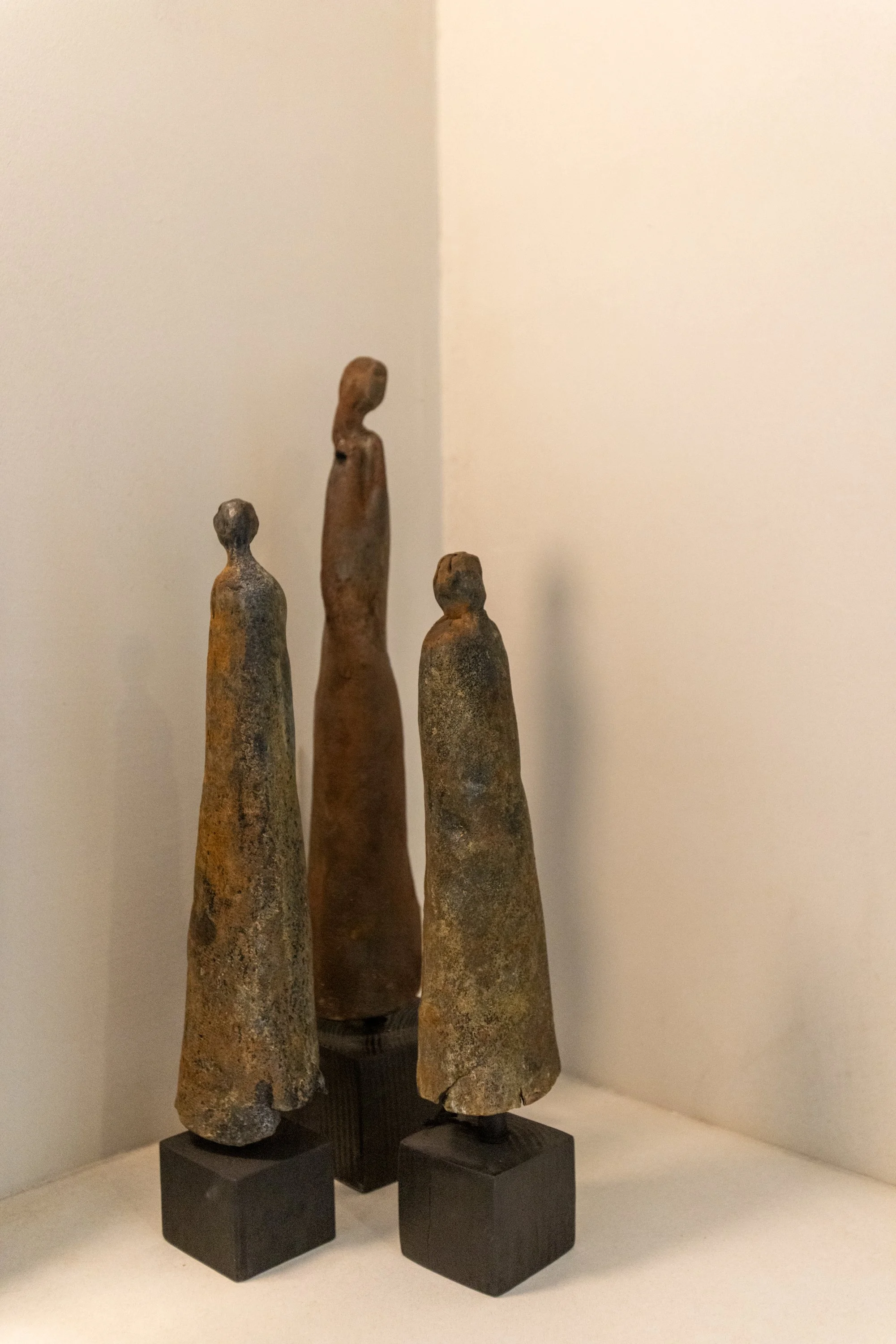 Three ancient clay figurines with elongated bodies and small heads on black bases displayed in a museum.