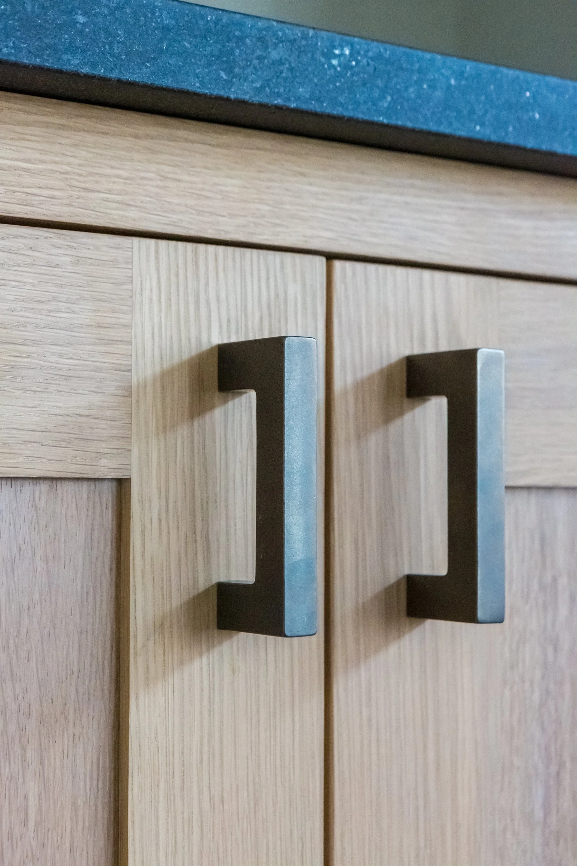 Close-up of two wooden cabinet handles with a portion of a blue countertop visible above them.