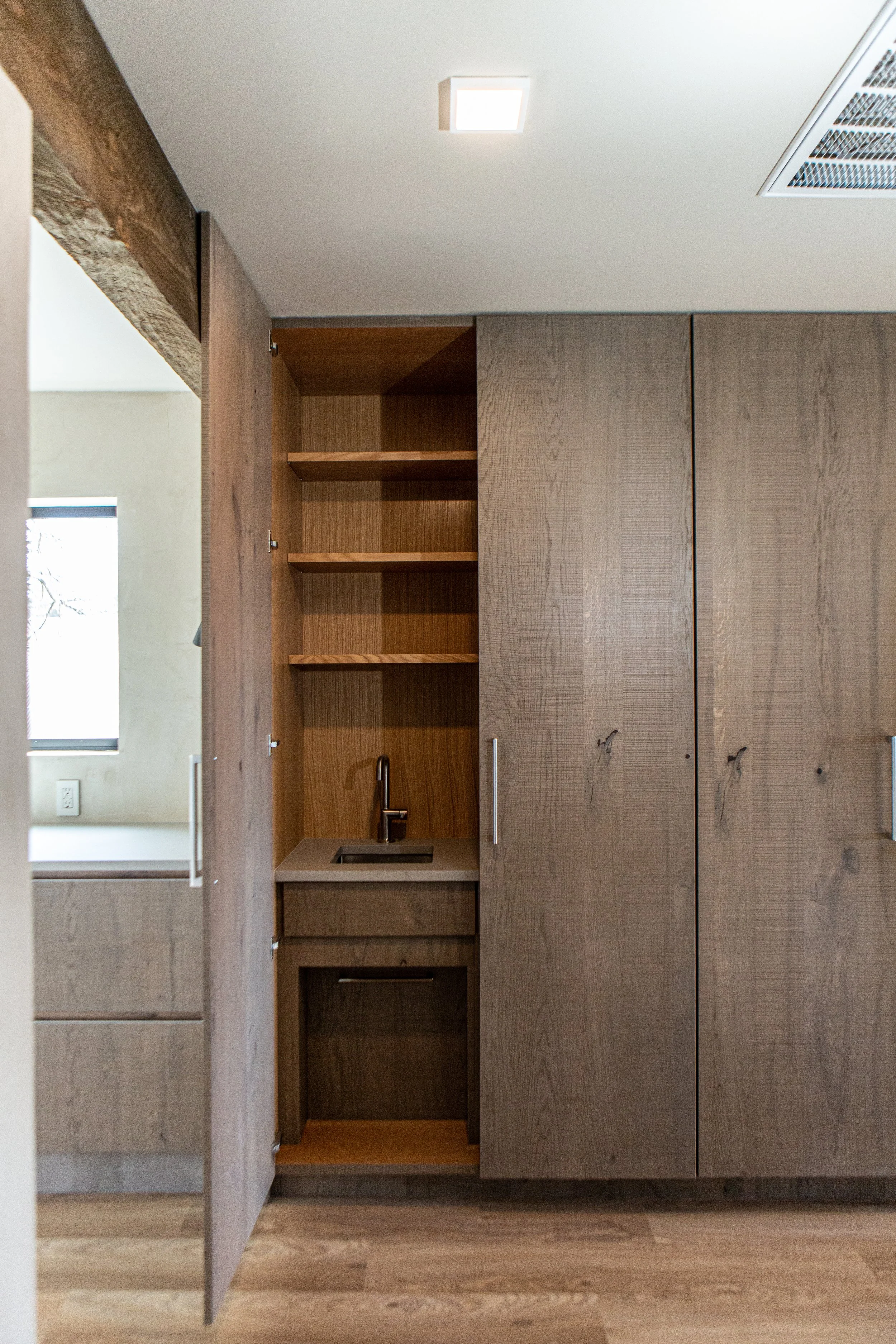Interior of a modern kitchen with wooden cabinets, an open shelf, a small sink, and a window with natural light.