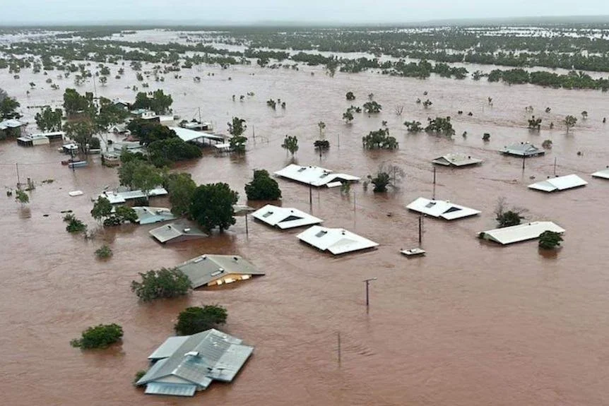 Flooded residential area with partially submerged houses and trees in muddy water.