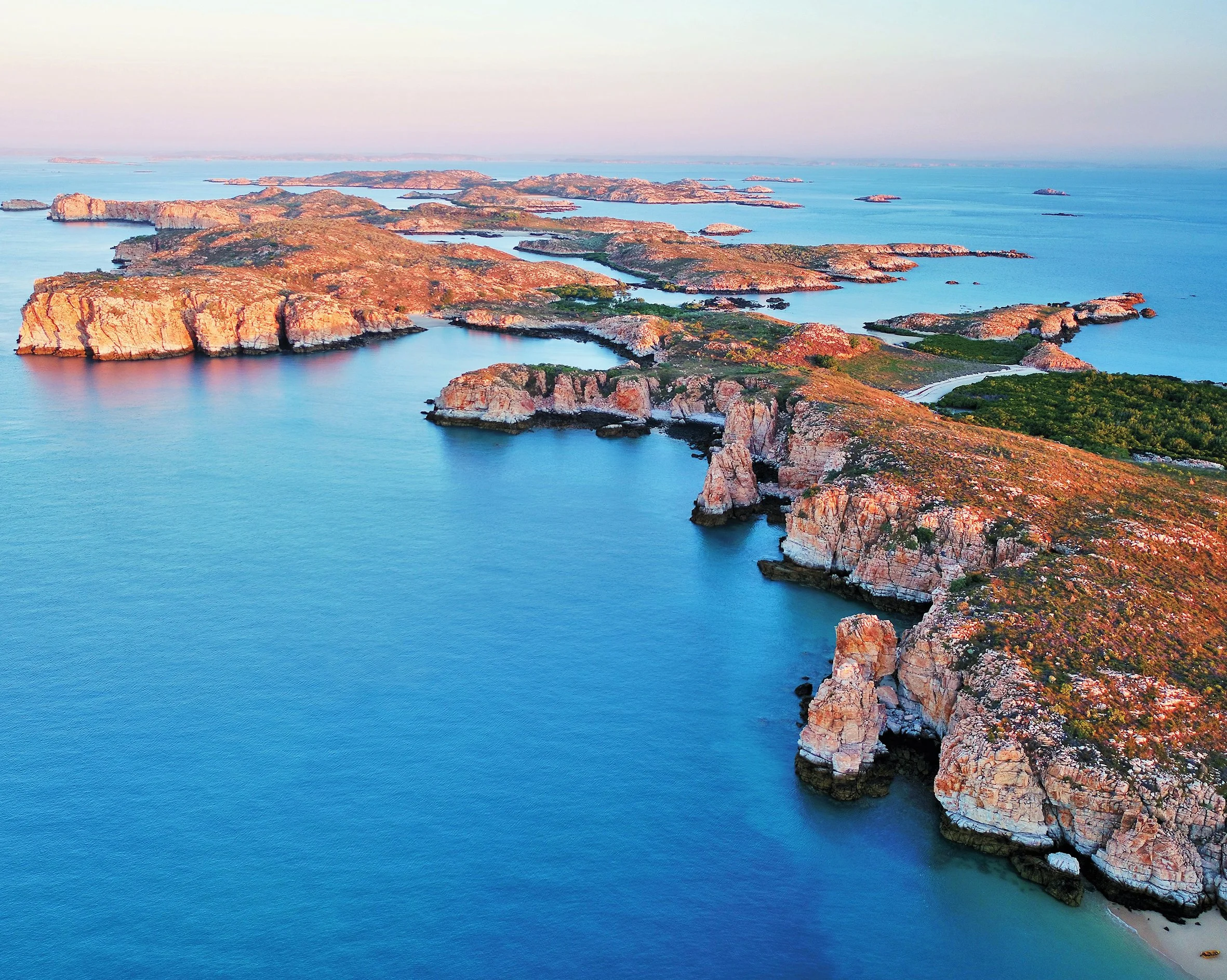 Aerial view of rocky island formations with water in between, during sunset or sunrise with warm light