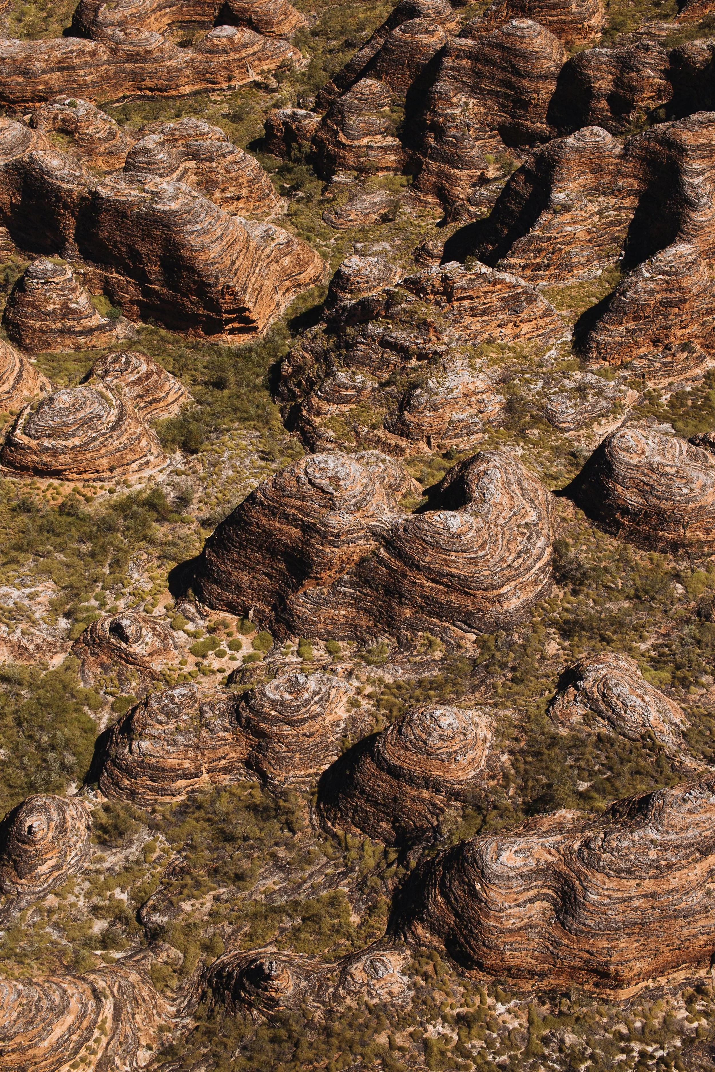 Aerial view of a rugged desert landscape with layered, rounded rock formations and sparse vegetation.