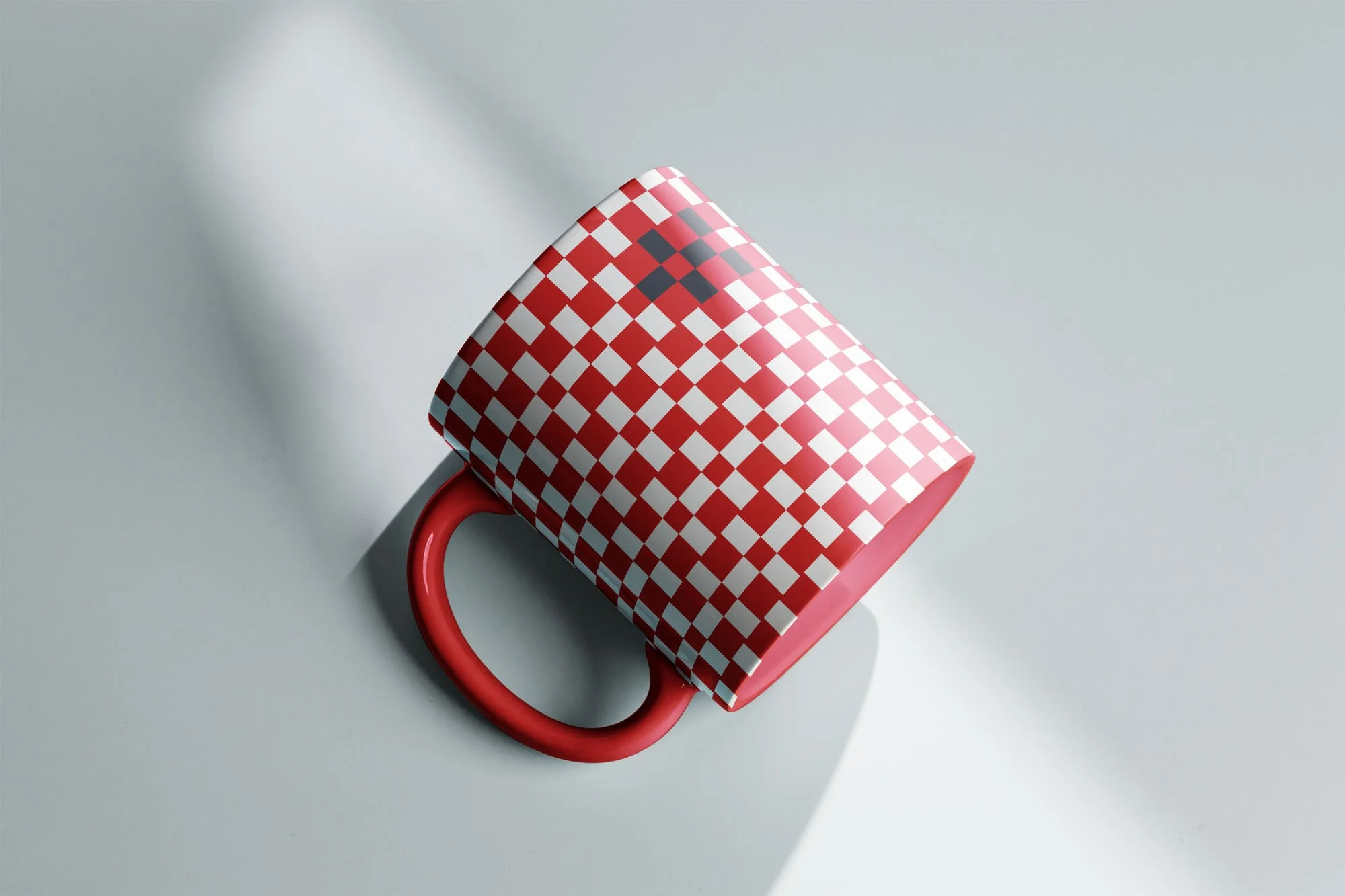Red mug with white checkered pattern on a light gray surface, casting a shadow.